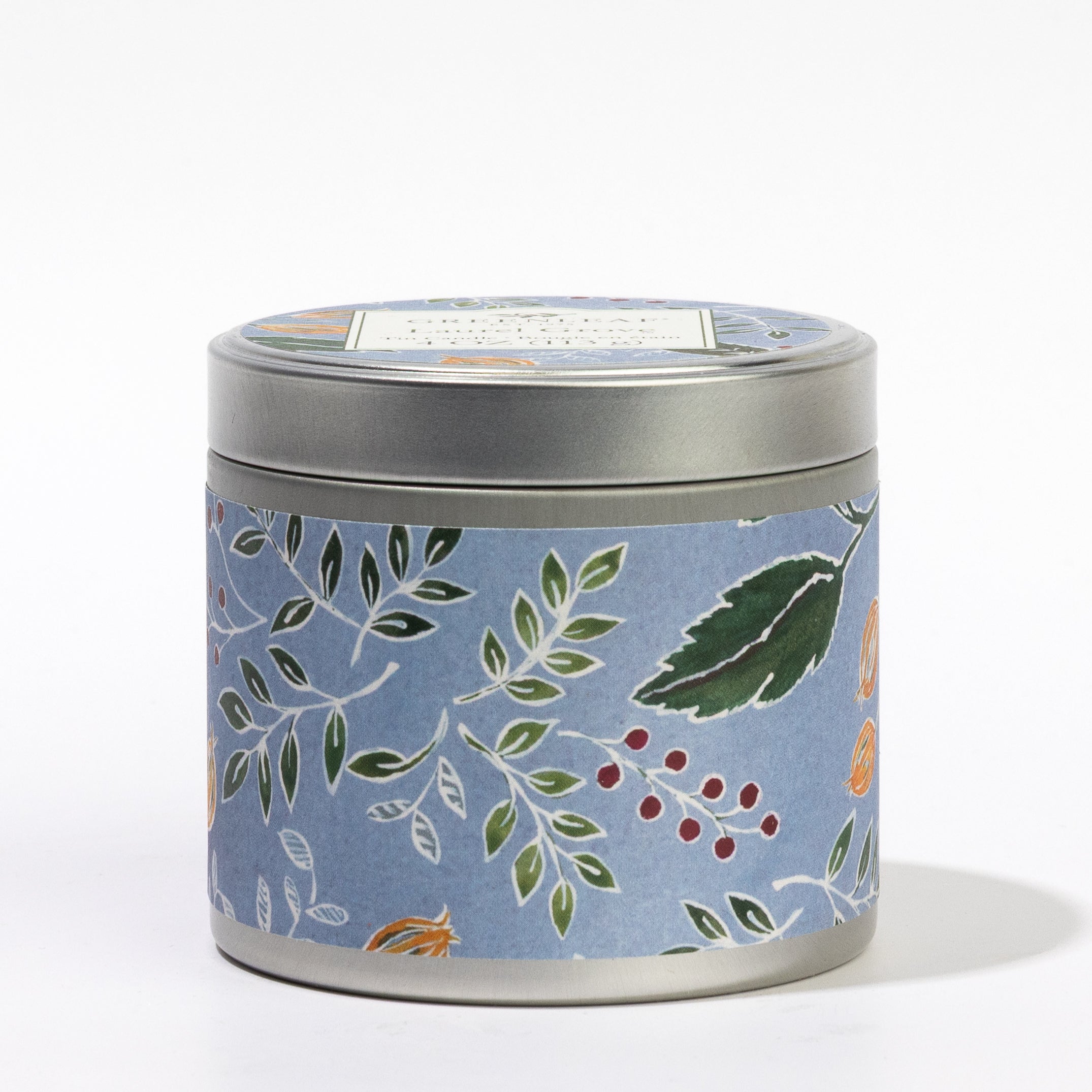 A round metal tin candle, the Laurel Grove Tin Candle by Greenleaf Gifts, features a blue label adorned with a leafy botanical pattern in green, red, and orange. Set against a plain white background, this charming travel candle captures the essence of Greenleaf fragrance for relaxation wherever you go.