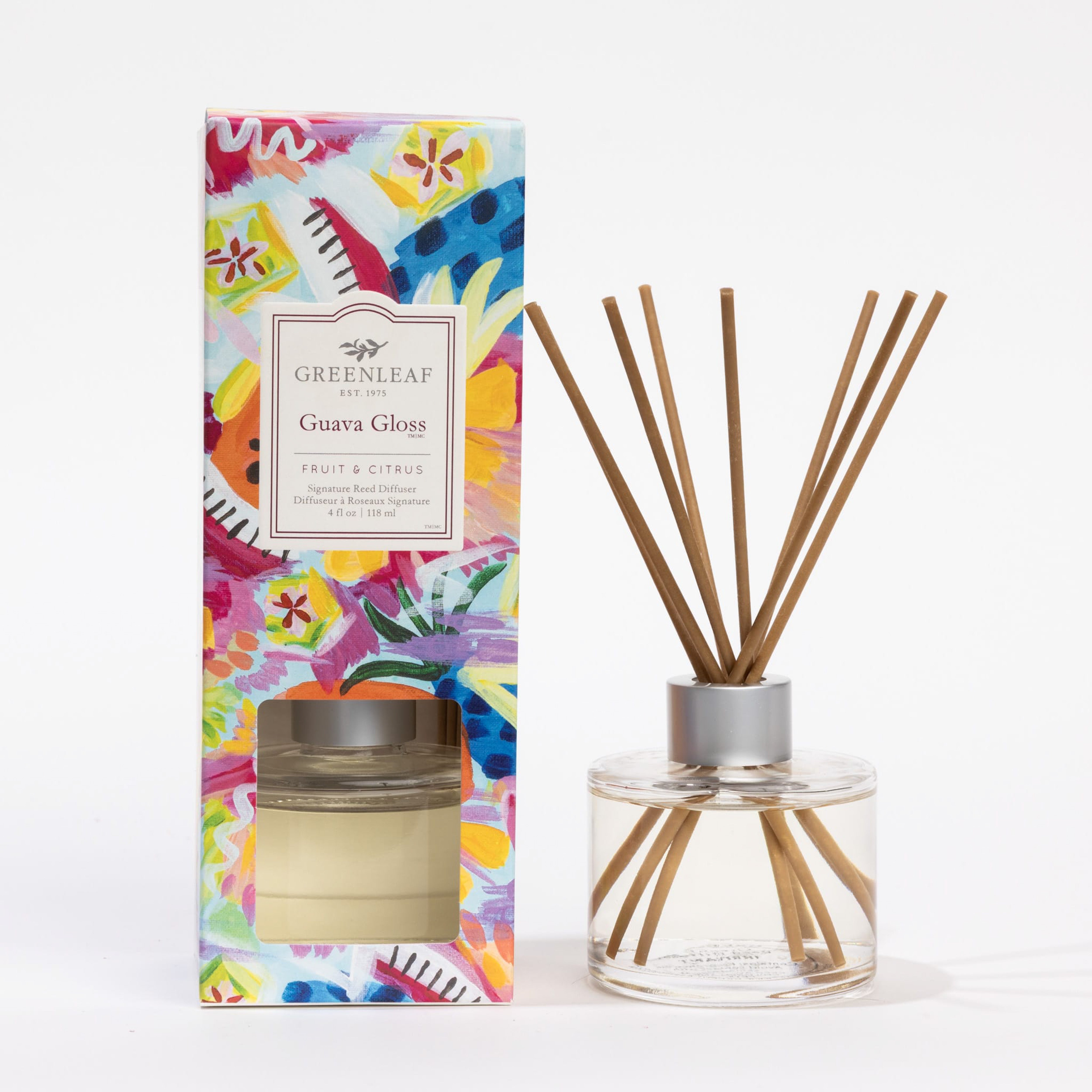 A Greenleaf Gifts Guava Gloss Reed Diffuser with fiber reeds is shown in a round glass bottle beside its vibrant, floral-patterned box, which includes the product label and a window displaying the diffuser inside.