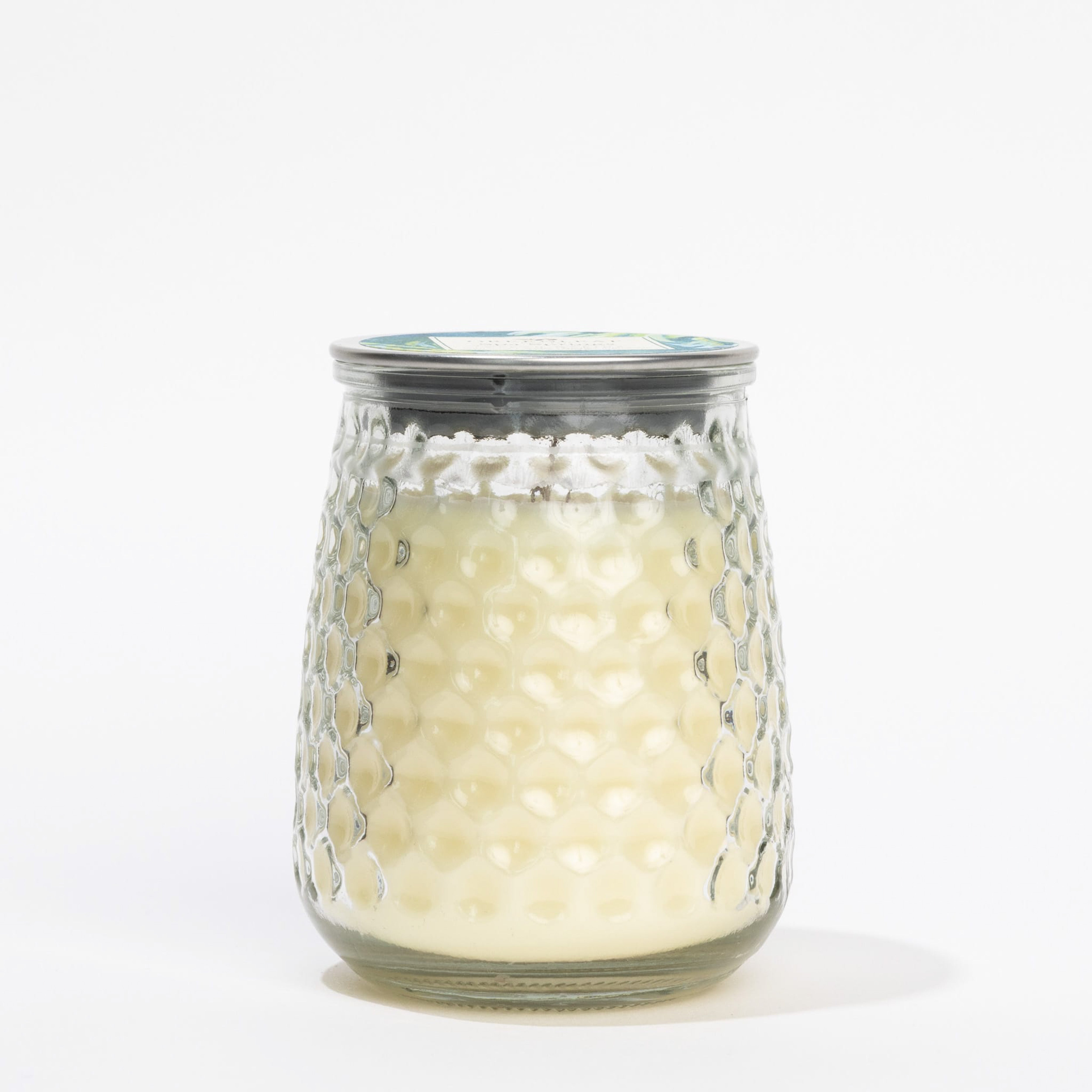 The Spa Springs Signature Candle by Greenleaf Gifts features a textured, honeycomb-patterned glass and a metal lid, radiating fresh elegance, and is photographed against a plain white background.