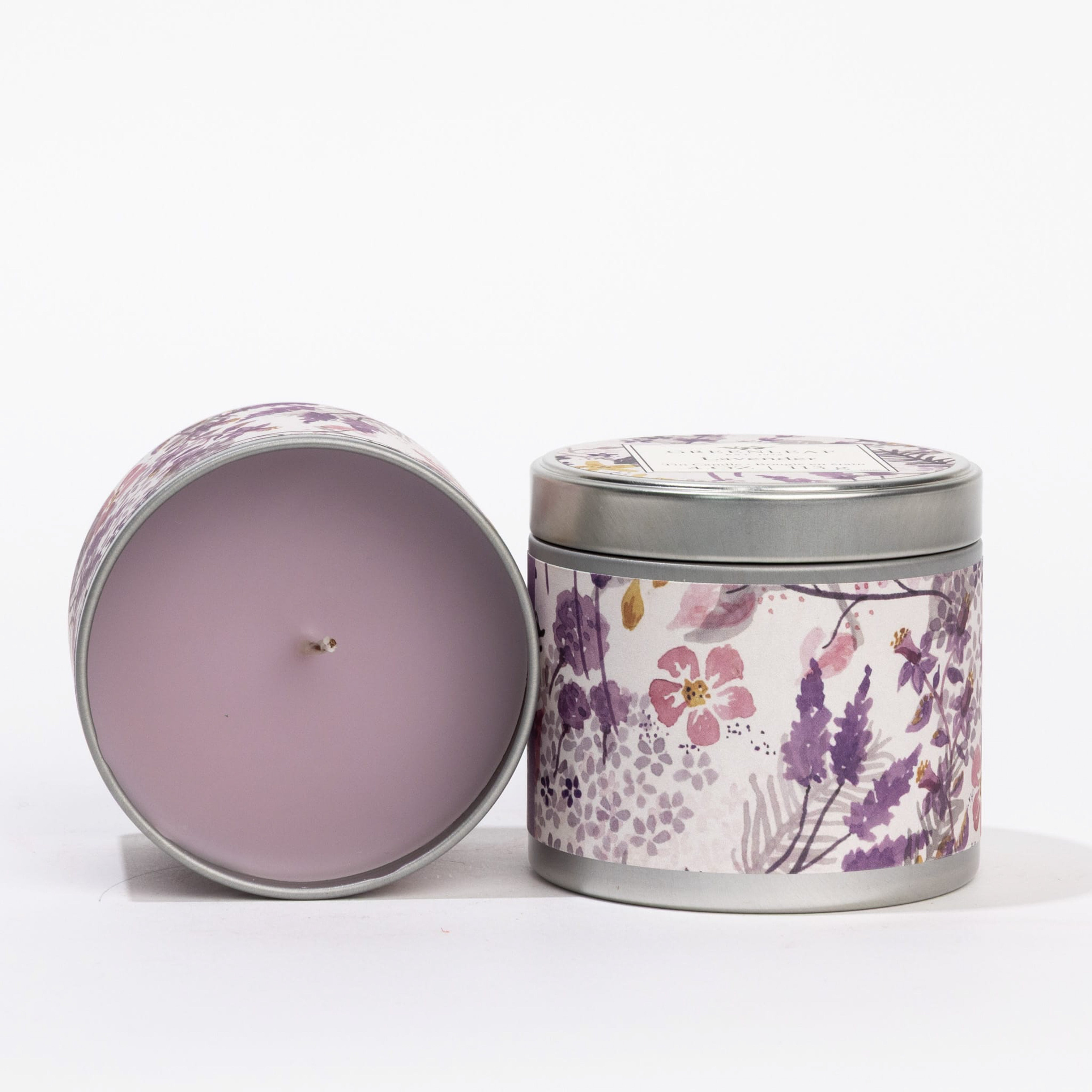 Two Greenleaf Gifts Lavender Tin Candles are shown: one open to reveal light purple wax, the other closed with a floral label featuring pink and purple flowers—both offer a lovely floral fragrance.