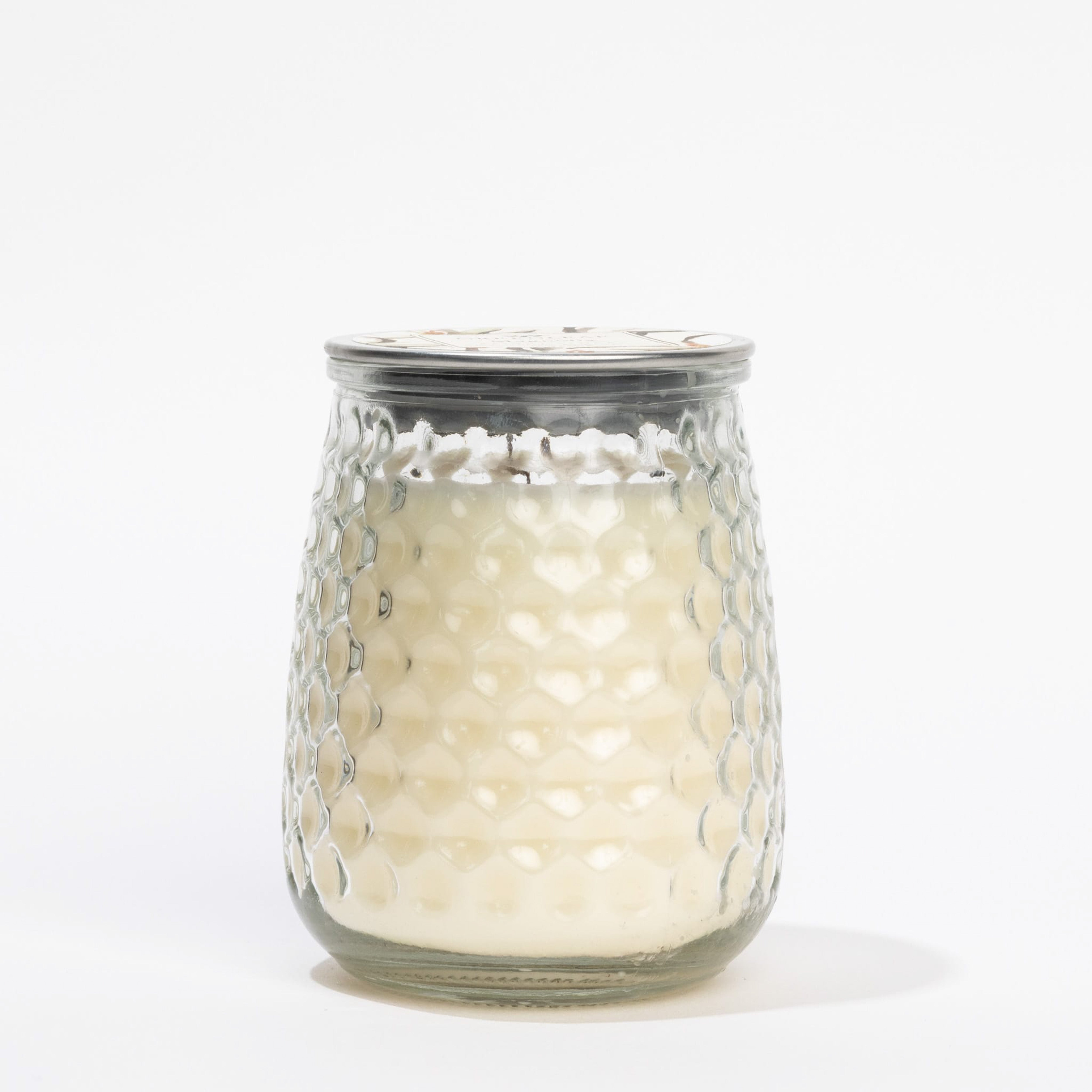 The Magnolia Signature Candle by Greenleaf Gifts is shown in a textured white hobnail glass jar with a metal lid, featuring a magnolia fragrance, displayed against a plain white background.