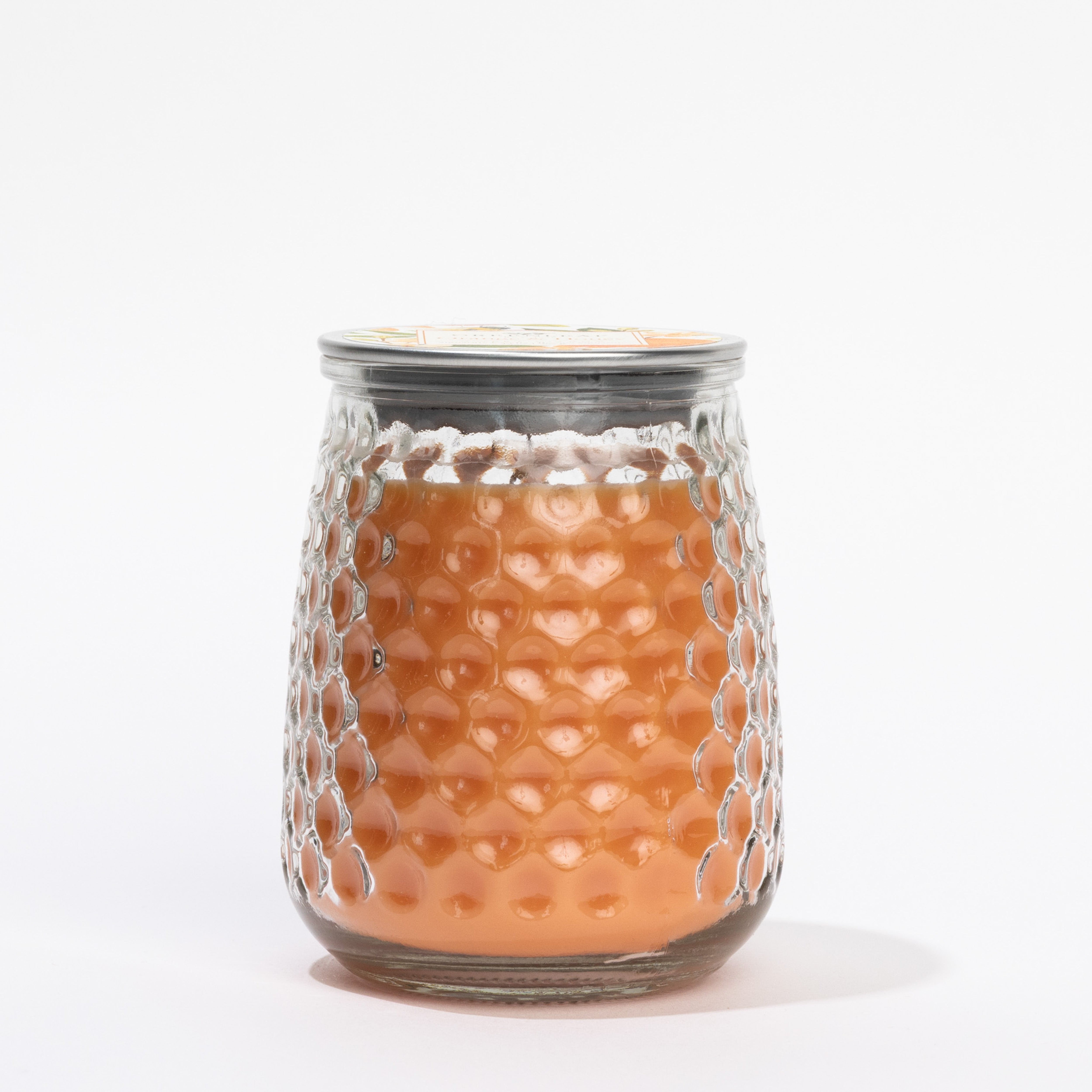 A clear glass jar with a honeycomb pattern, filled with light amber wax and sealed with a metal lid, showcases the Orange & Honey Signature Candle by Greenleaf Gifts against a plain white background.