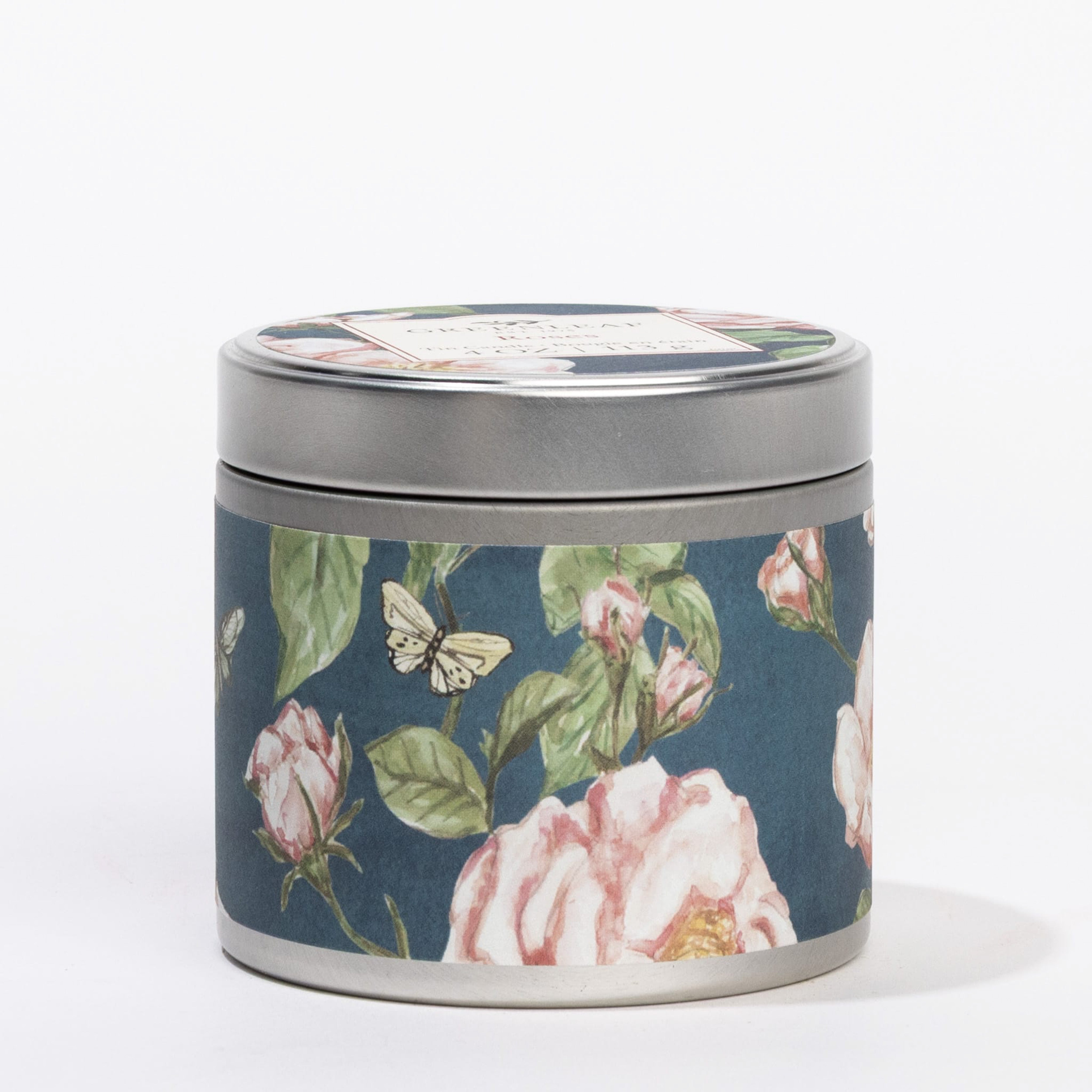 The Roses Tin Candle by Greenleaf Gifts is a portable candle in a round tin featuring pink flowers and butterflies on dark blue, with a silver lid. Its decor hints at the delightful roses fragrance inside.