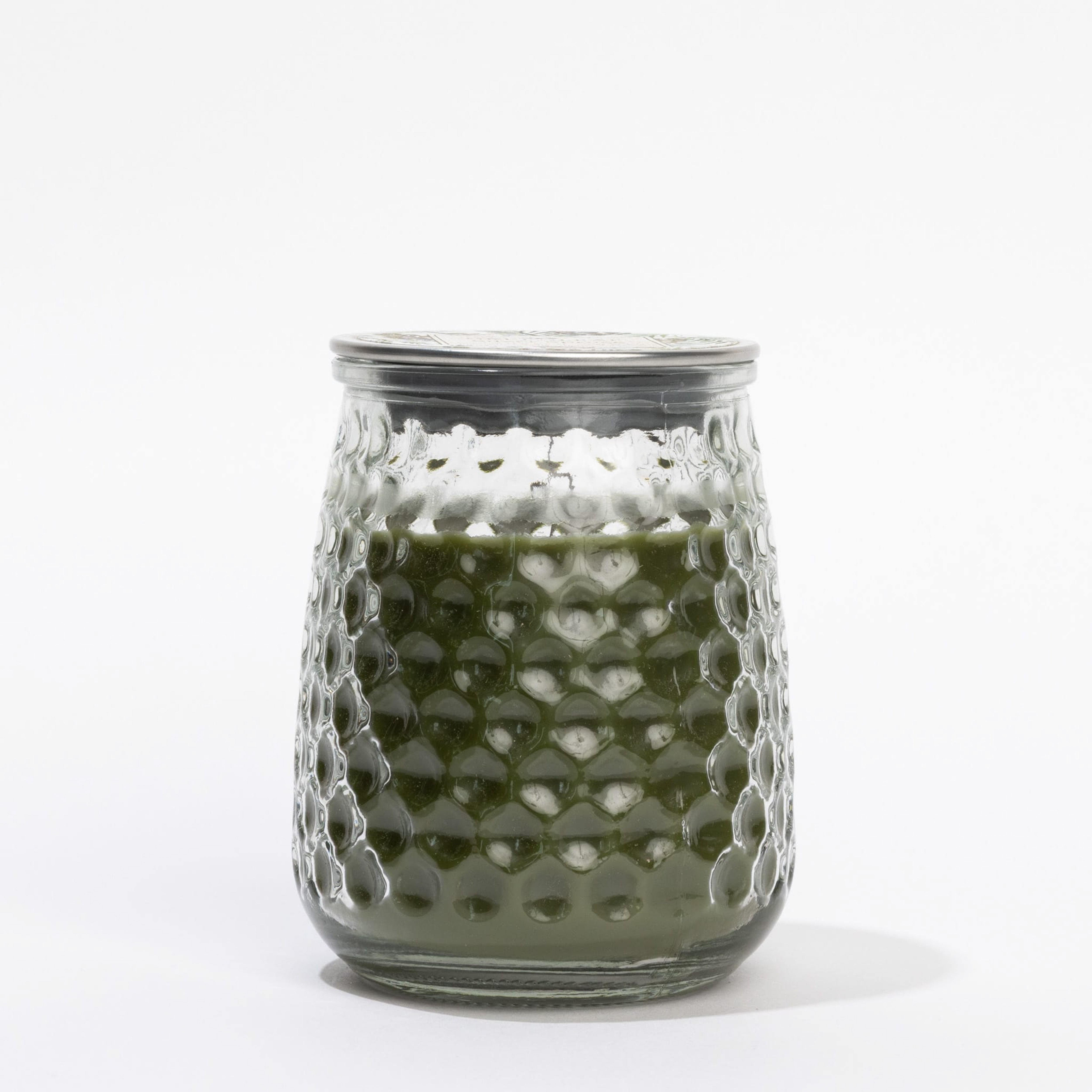 A clear, textured glass jar with a metal lid holds Greenleaf Gifts’ Silver Spruce Signature Candle, filled with green wax and featuring a refreshing scent, displayed against a plain white background.