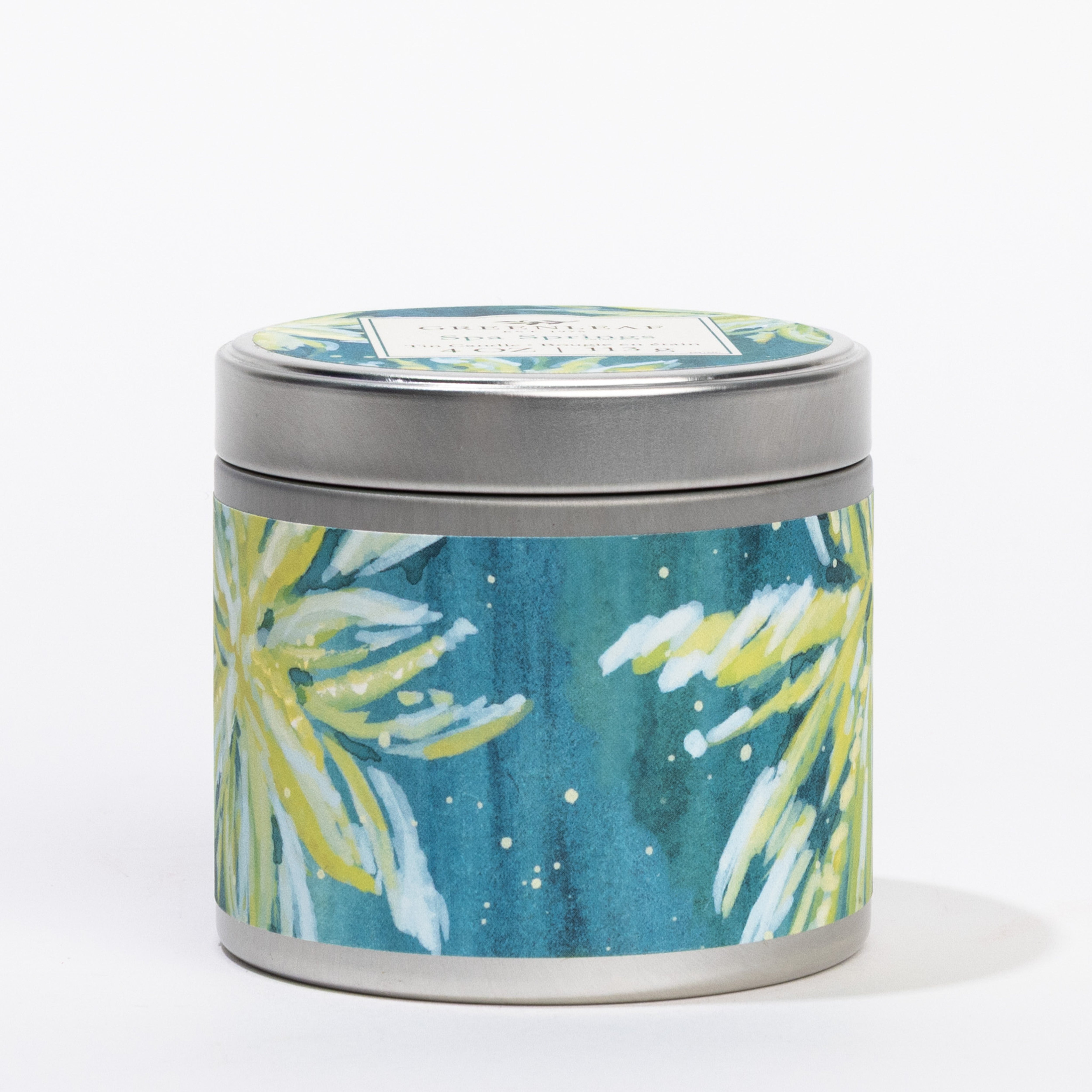 The Spa Springs Tin Candle by Greenleaf Gifts features a round tin with yellow and green floral designs on a blue background, a silver lid with a rectangular label, and is perfect for spa-like relaxation anywhere.