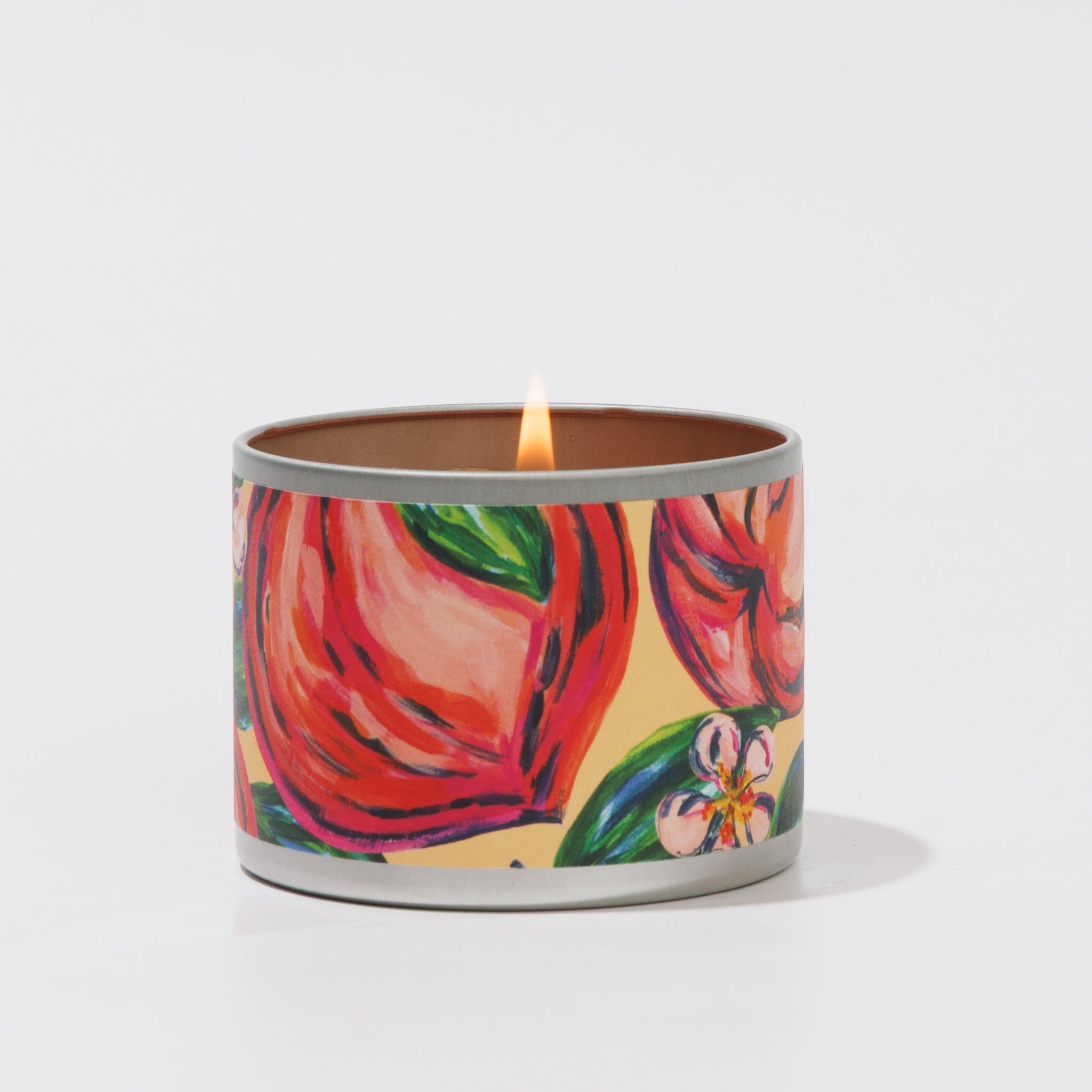 The Coco Peach Tin Candle by Greenleaf Gifts comes in a round metal tin with a vibrant hand-painted design of pink and red flowers and green leaves on a peach background, making it a stylish and portable choice for any space.