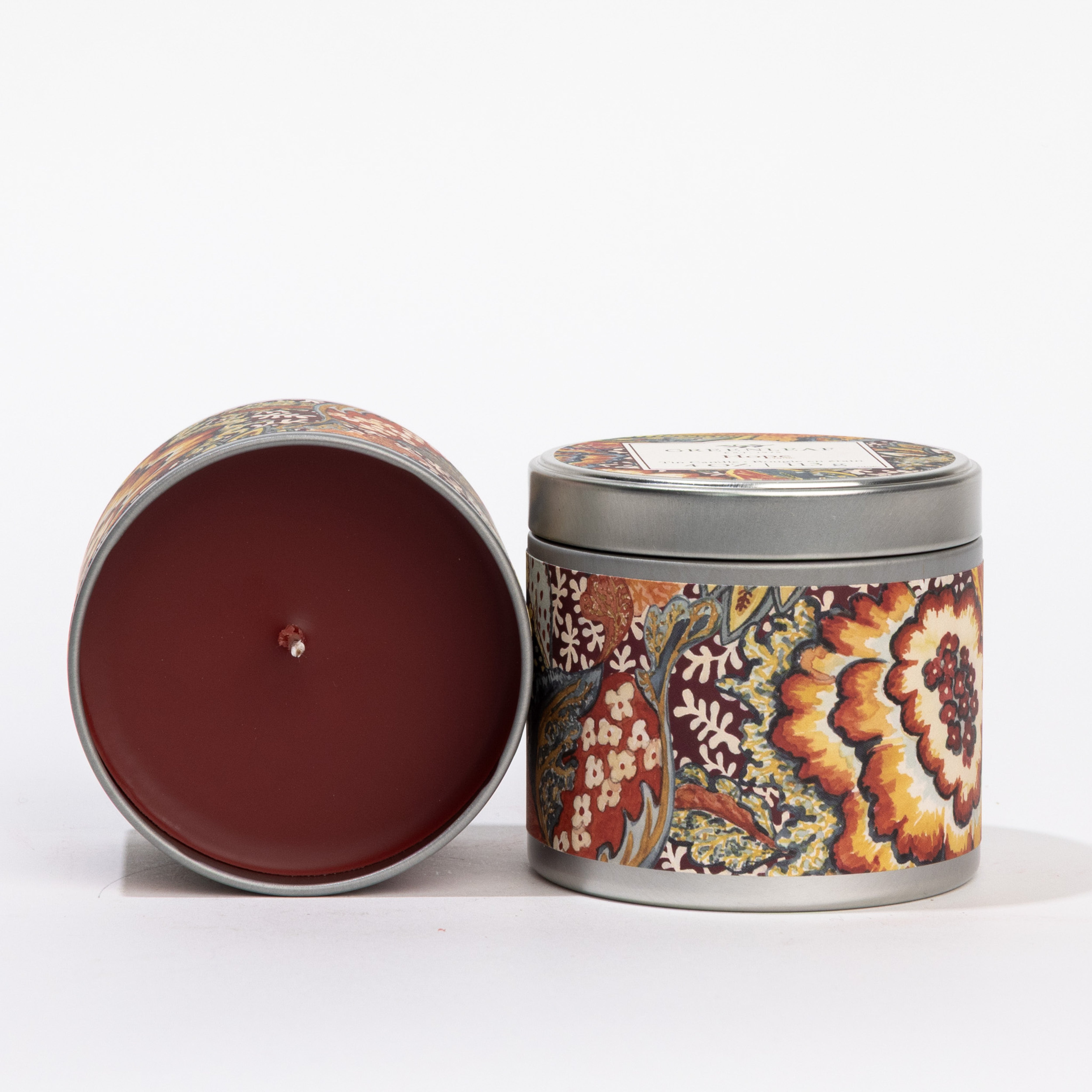 Two Hope Tin Candles by Greenleaf Gifts, each with colorful floral patterns—one upright with a lid, one on its side showing a dark red candle. Both add cozy home fragrance with their decorative designs.