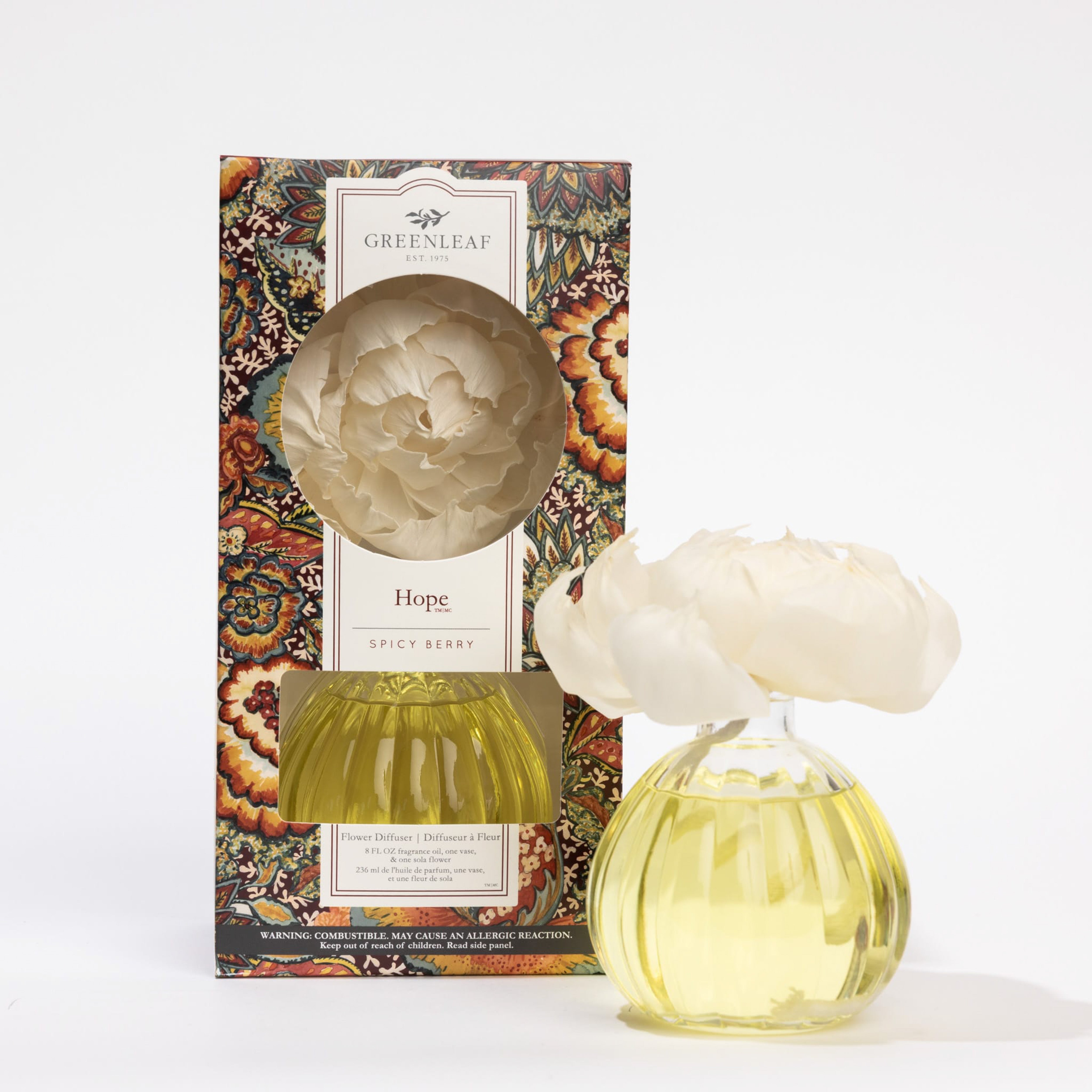 The Greenleaf Gifts Hope Flower Diffuser features an 8 oz yellow liquid, a white flower topper, and lasts up to 60 days. It sits beside its decorative floral-patterned box with a round window, labeled "Hope" by Greenleaf Gifts.