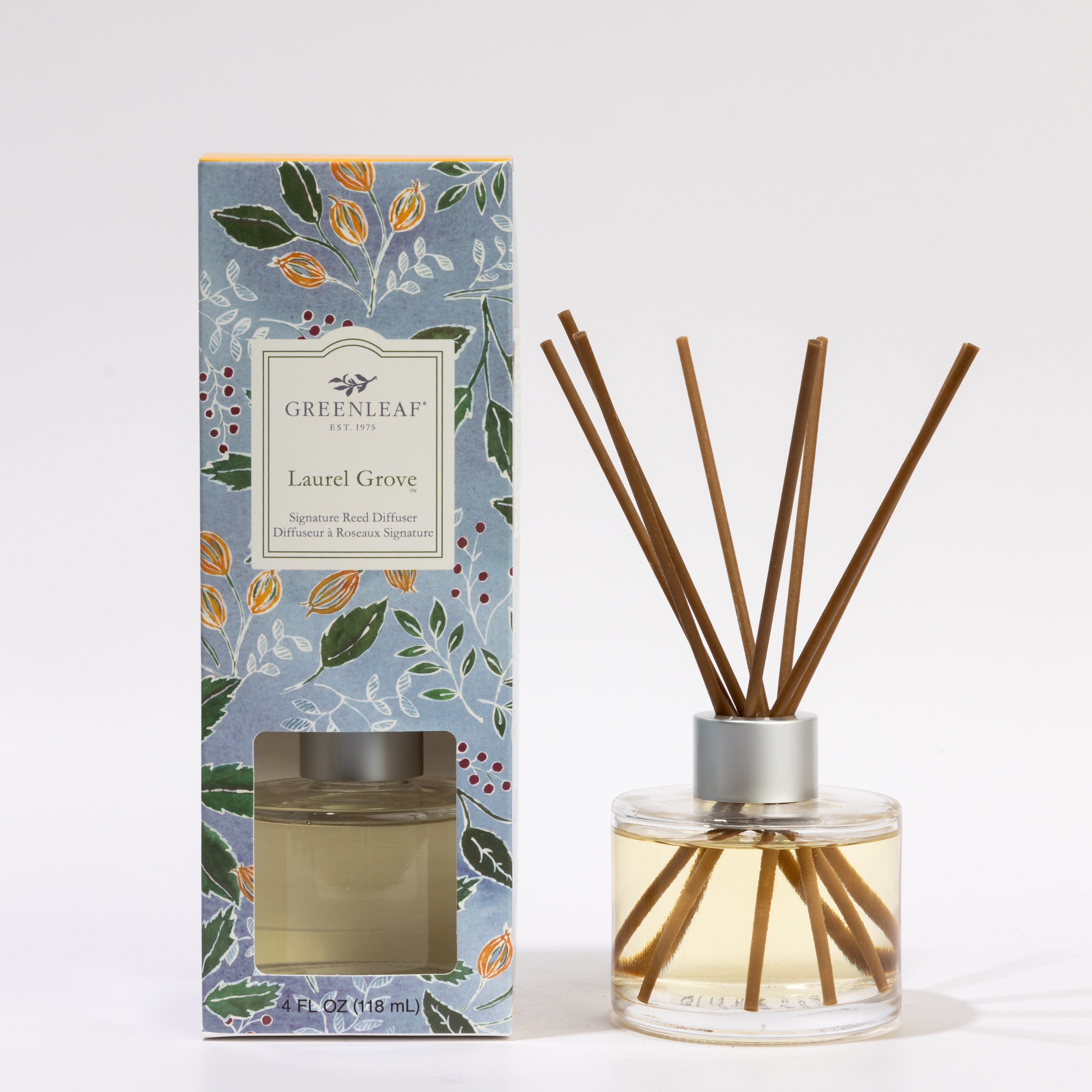 A Greenleaf Gifts Laurel Grove Reed Diffuser, 4 oz, with wooden sticks in a round glass bottle is shown beside its blue floral-patterned box. Enjoy up to 30 days of fragrance.