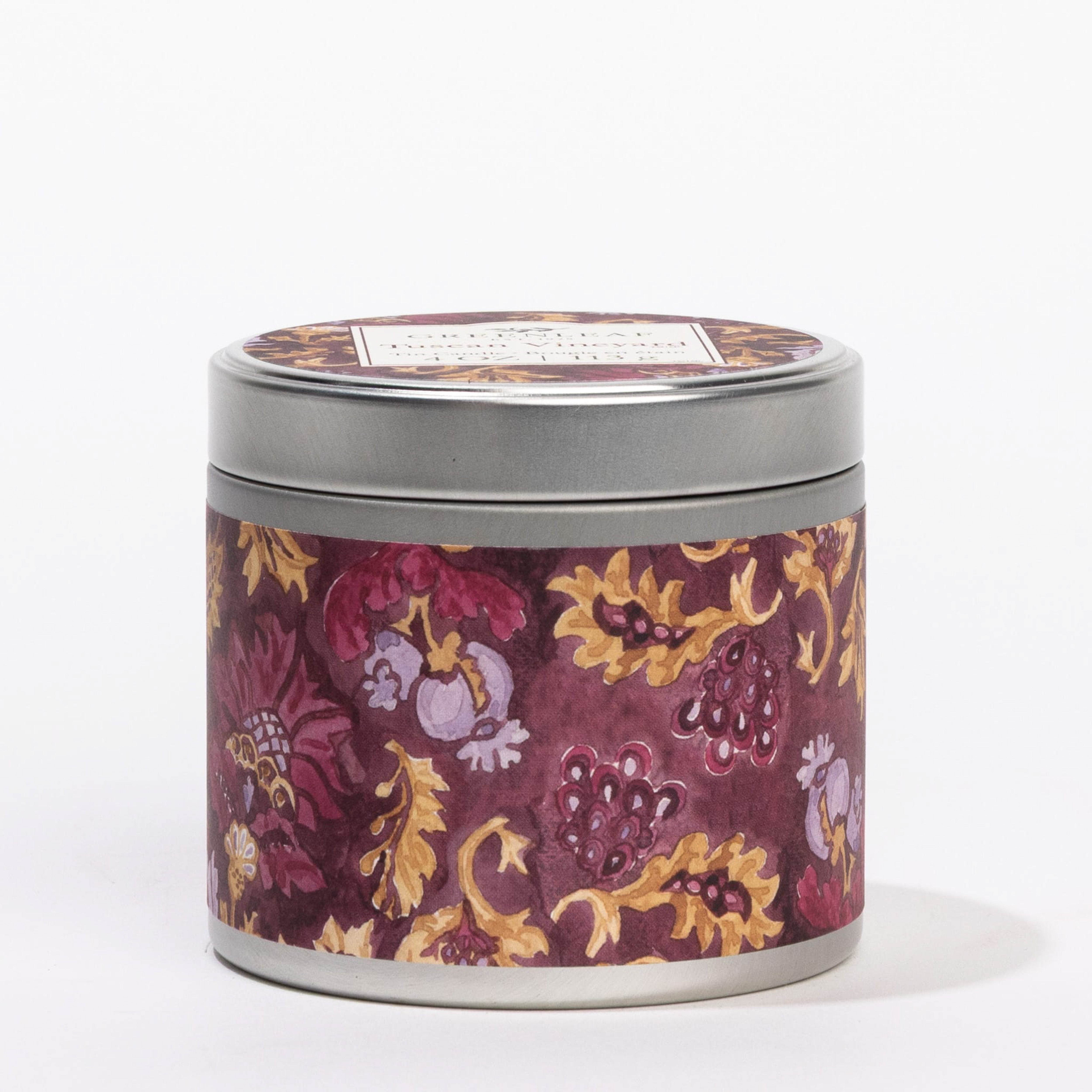 The Greenleaf Gifts Tuscan Vineyard Tin Candle features a maroon label with yellow and purple floral patterns. This portable round metal tin has a lid and is shown against a white background.