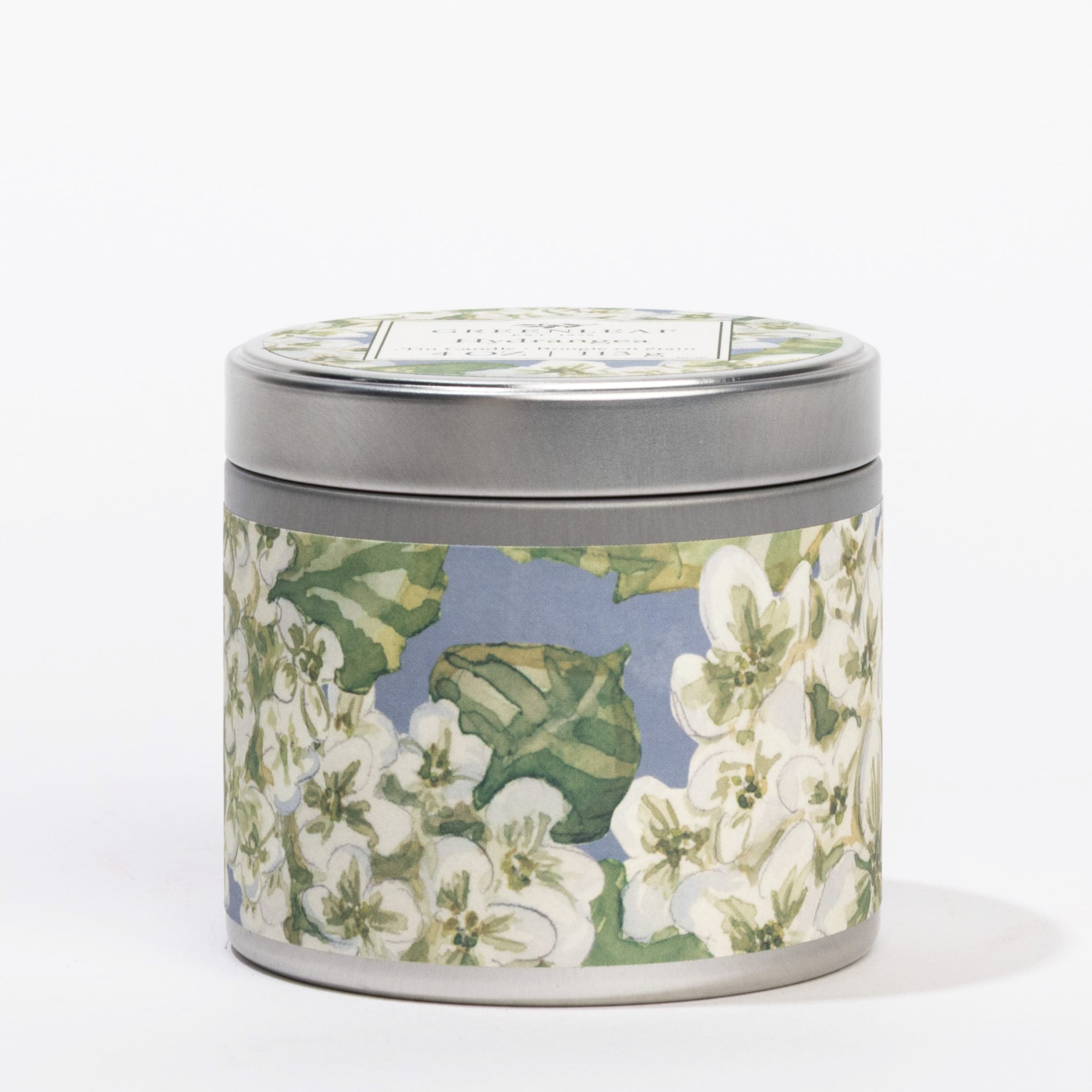The Hydrangea Tin Candle by Greenleaf Gifts features a floral design with white blossoms and green leaves on a blue tin. Ideal for travel, it infuses spaces with a refreshing hydrangea scent.