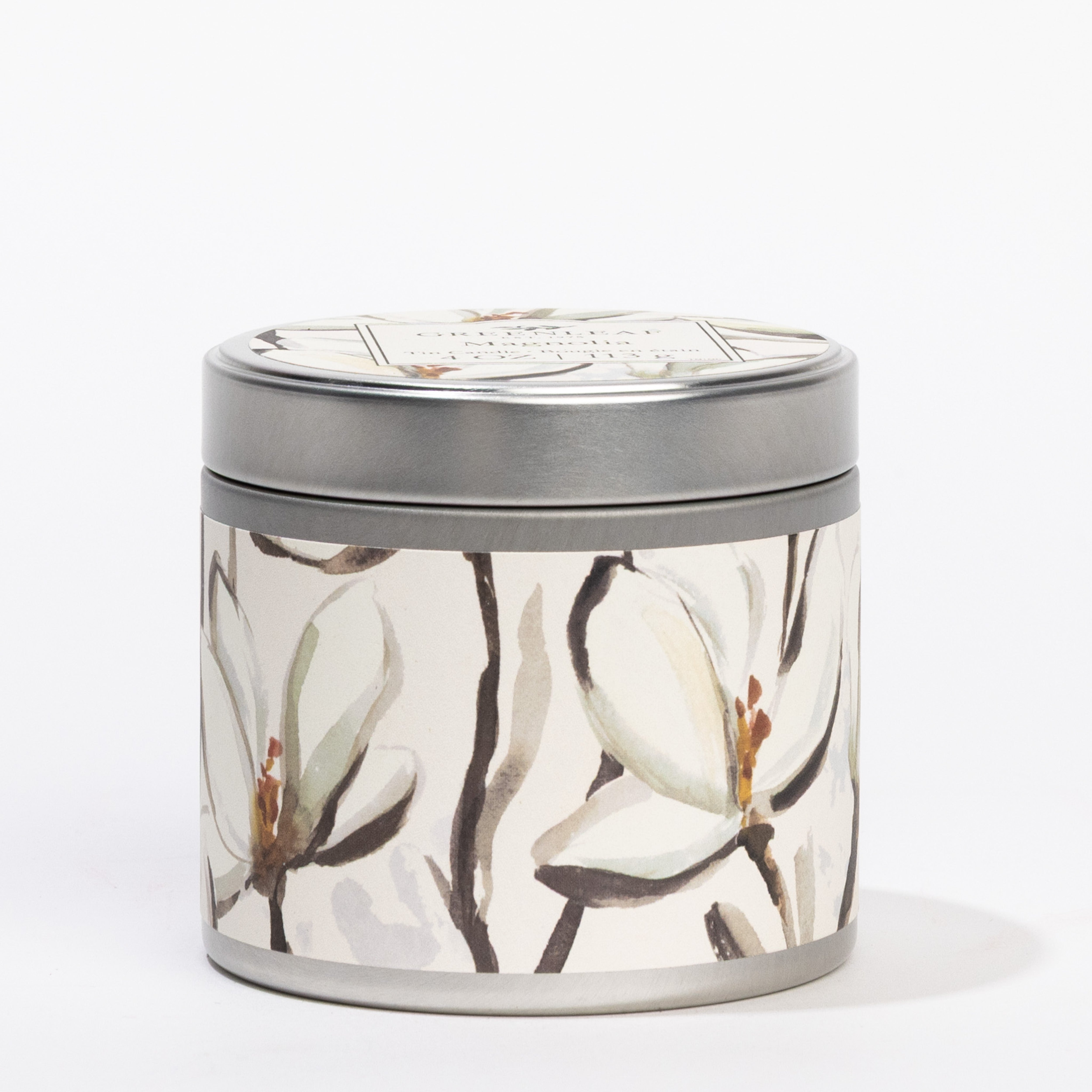 The Magnolia Tin Candle by Greenleaf Gifts features a round tin with a lid, adorned with white magnolia flowers and brown stems. Portable and stylish, its perfect for enjoying soothing magnolia fragrance wherever you go.