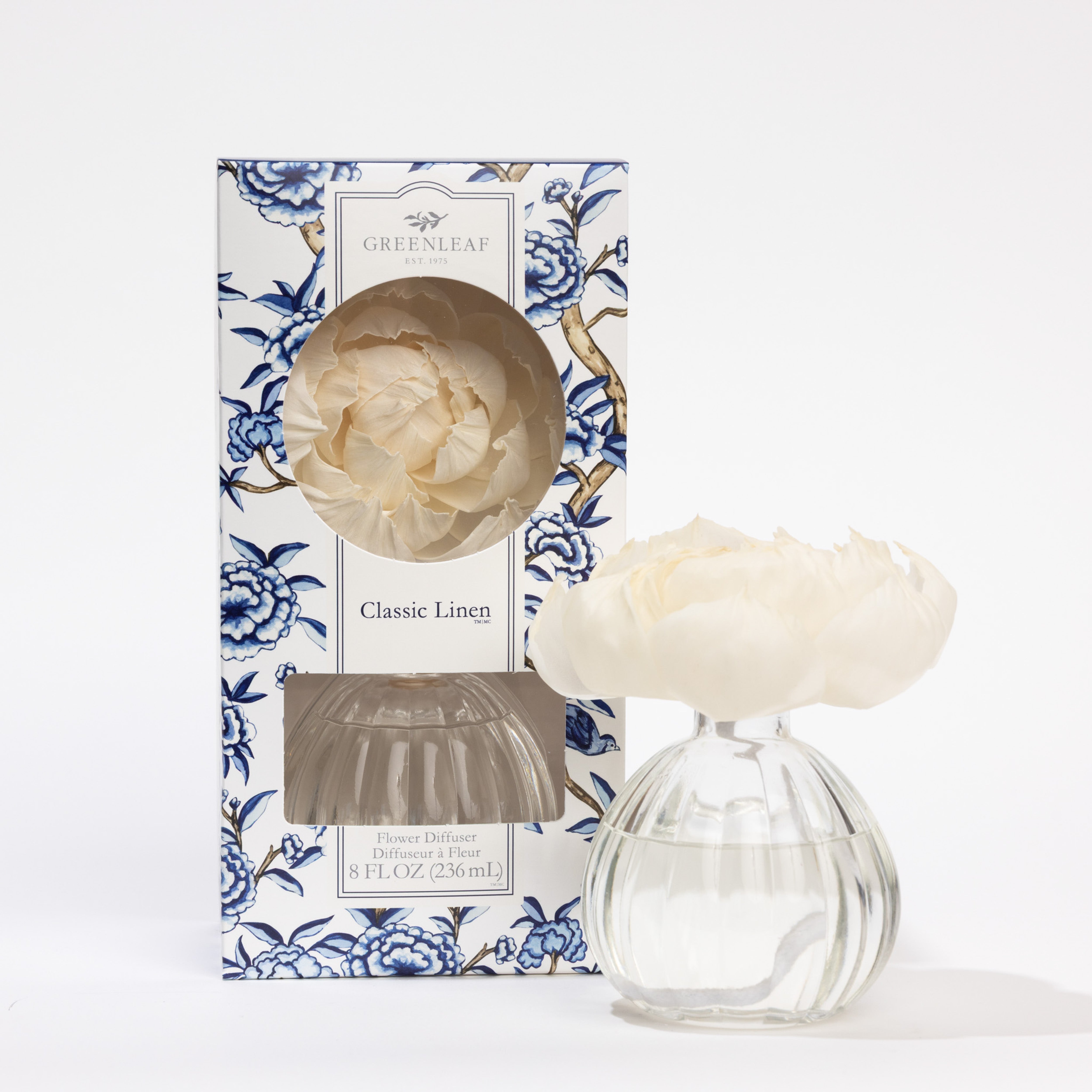 The Greenleaf Gifts Flower Diffuser-Classic Linen (8 oz, GLG966498S) includes a glass vase with clear liquid and a white artificial flower. Enjoy up to 60 days of fragrance, presented in a blue and white floral-patterned box.