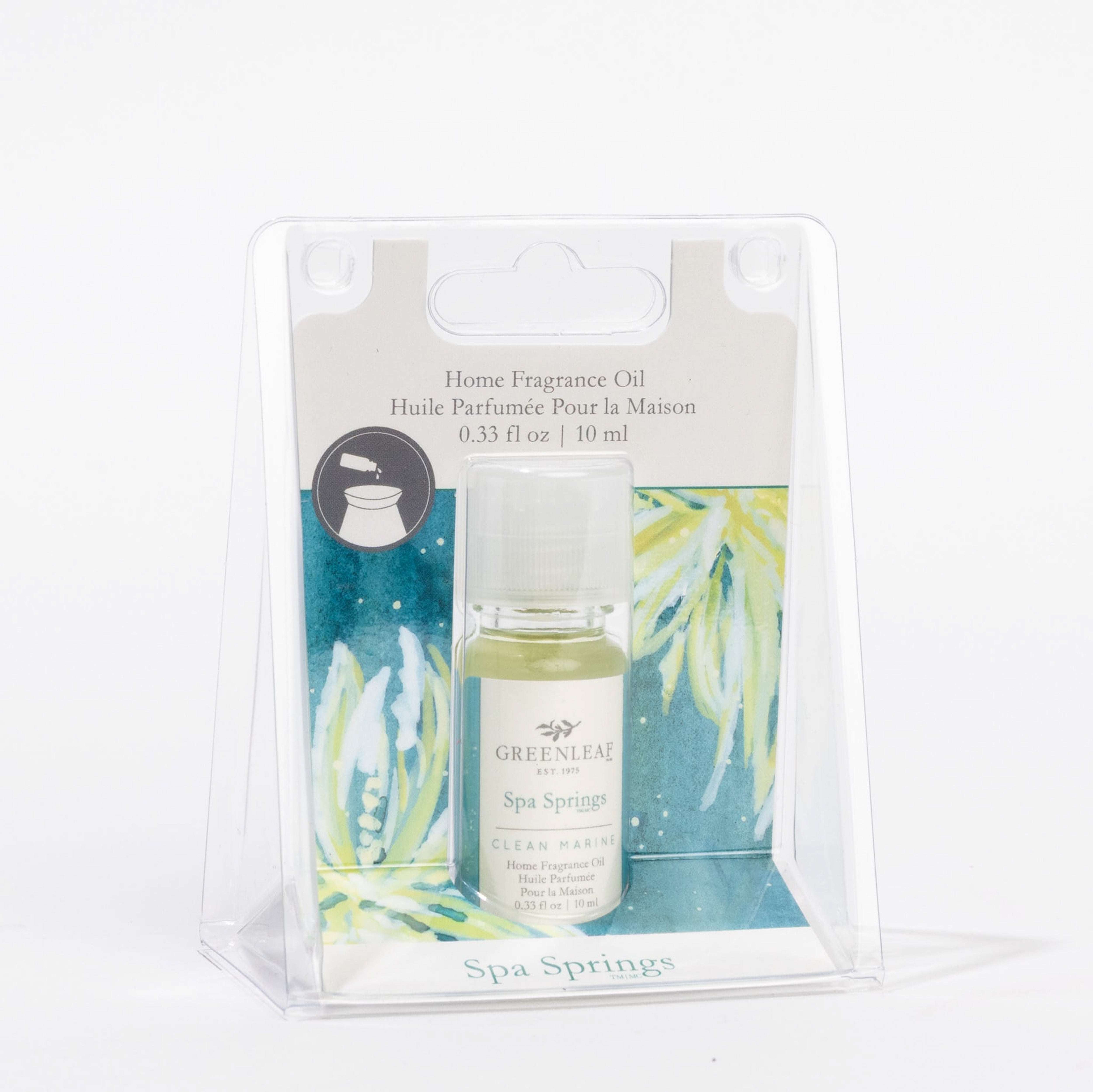 A small bottle of Greenleaf Gifts Spa Springs Home Fragrance Oil sits in clear plastic packaging, offering a flameless scent experience with a blue and green decorative insert and product details on the label.