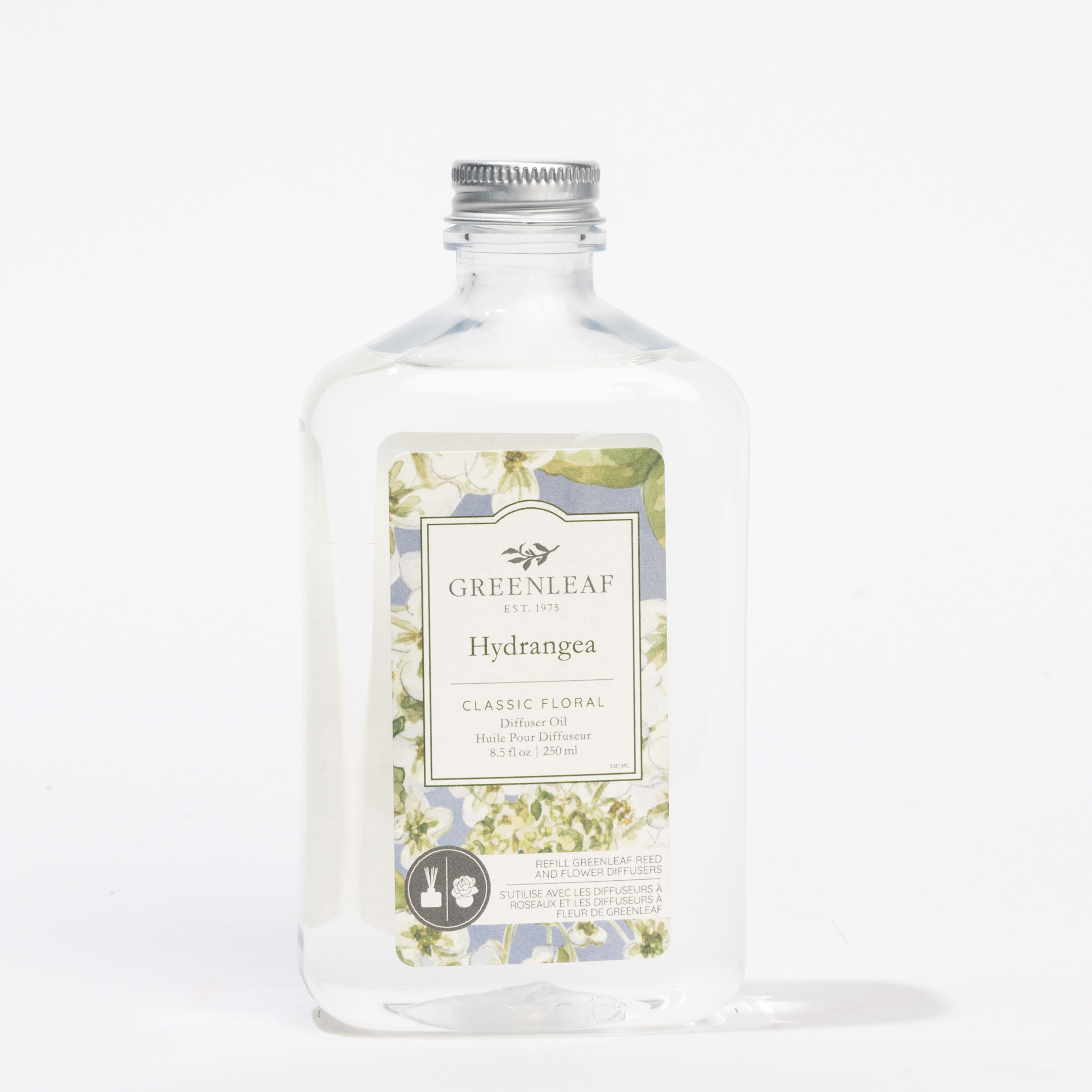 A clear bottle of Greenleaf Gifts Hydrangea Diffuser Refill Oil with a silver cap features a floral label with green and white hydrangea illustrations—ideal as replacement oil for reed diffusers.