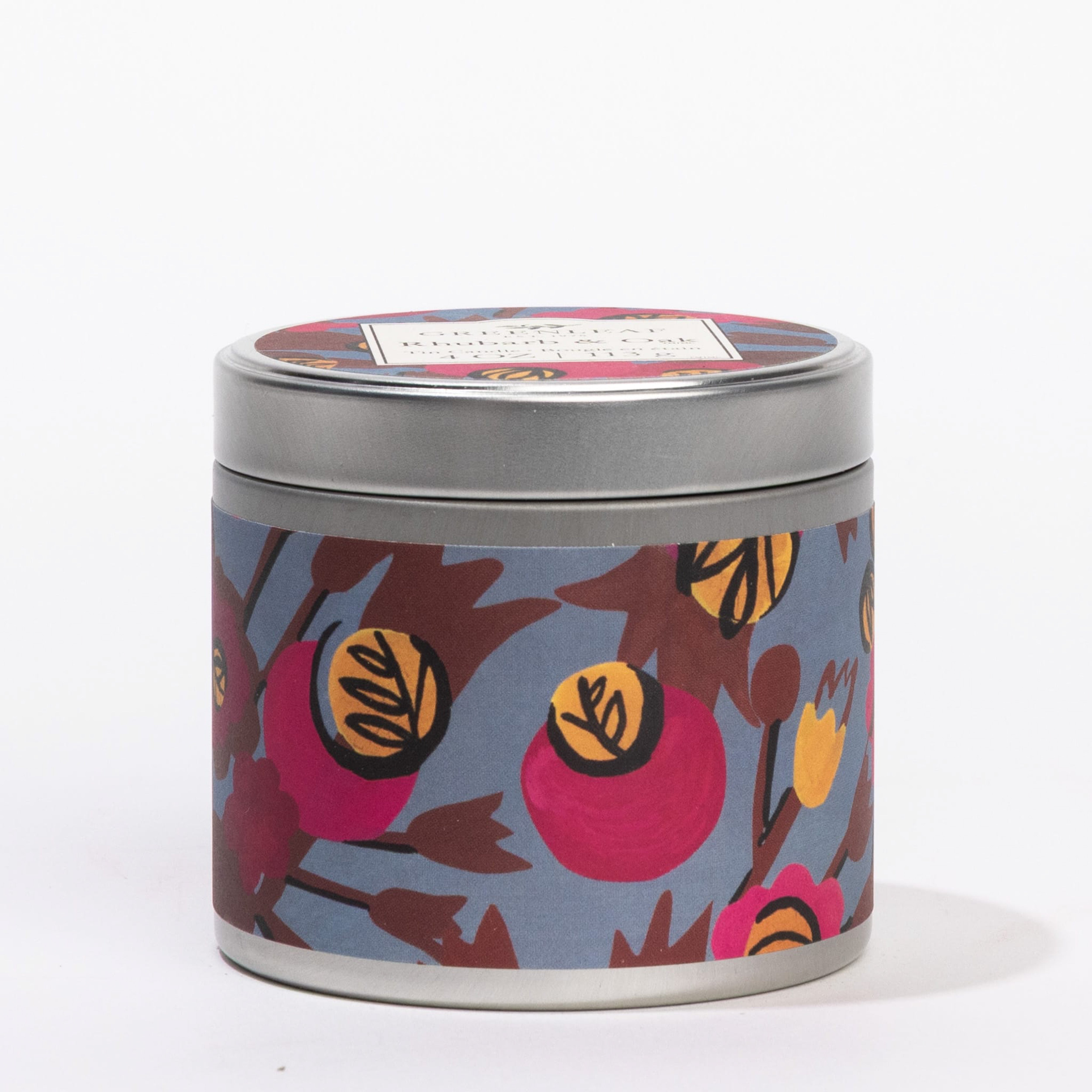 The Greenleaf Gifts Rhubarb & Oak Tin Candle features a round portable tin with a silver lid, a blue floral design with red, yellow, and orange flowers, and a rectangular label showcasing its rhubarb & oak scent.