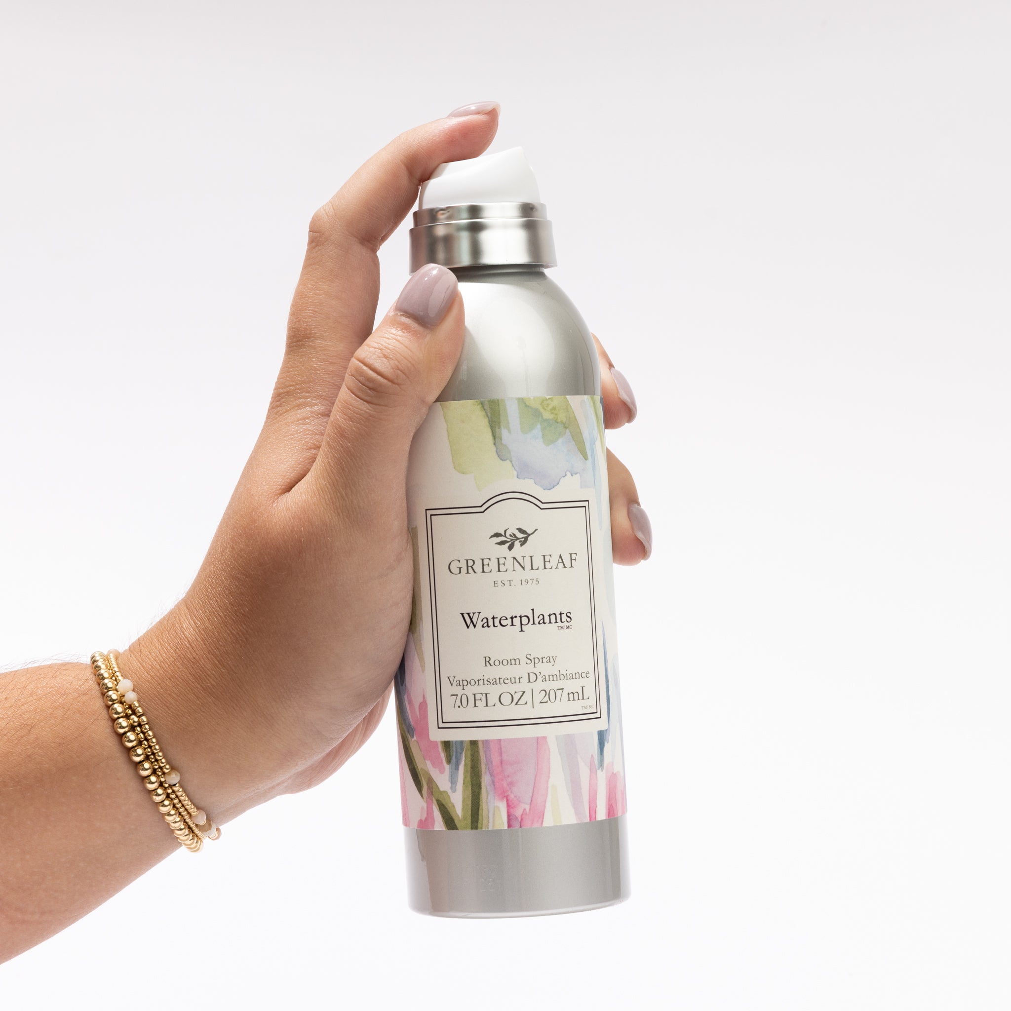 A hand holds a silver bottle of Greenleaf Gifts Waterplants Room Spray with a floral label design, set against a plain white background.