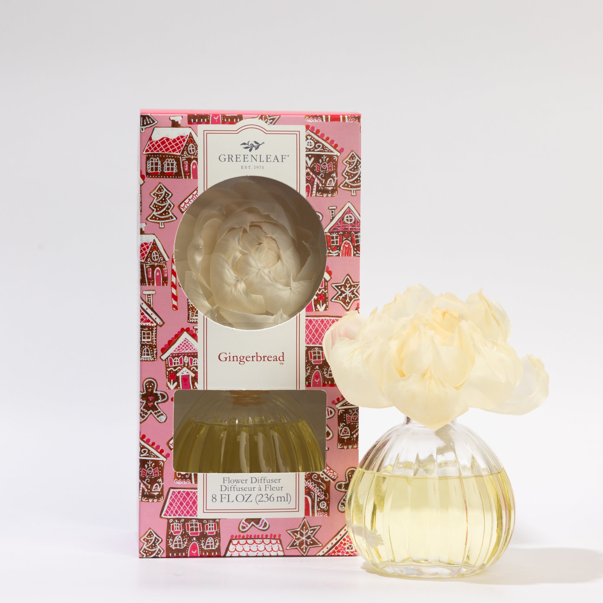 The Greenleaf Gifts Gingerbread Flower Diffuser comes in a decorative gingerbread house box with a clear glass vase holding yellow oil and a white sola paper flower for fragrance.