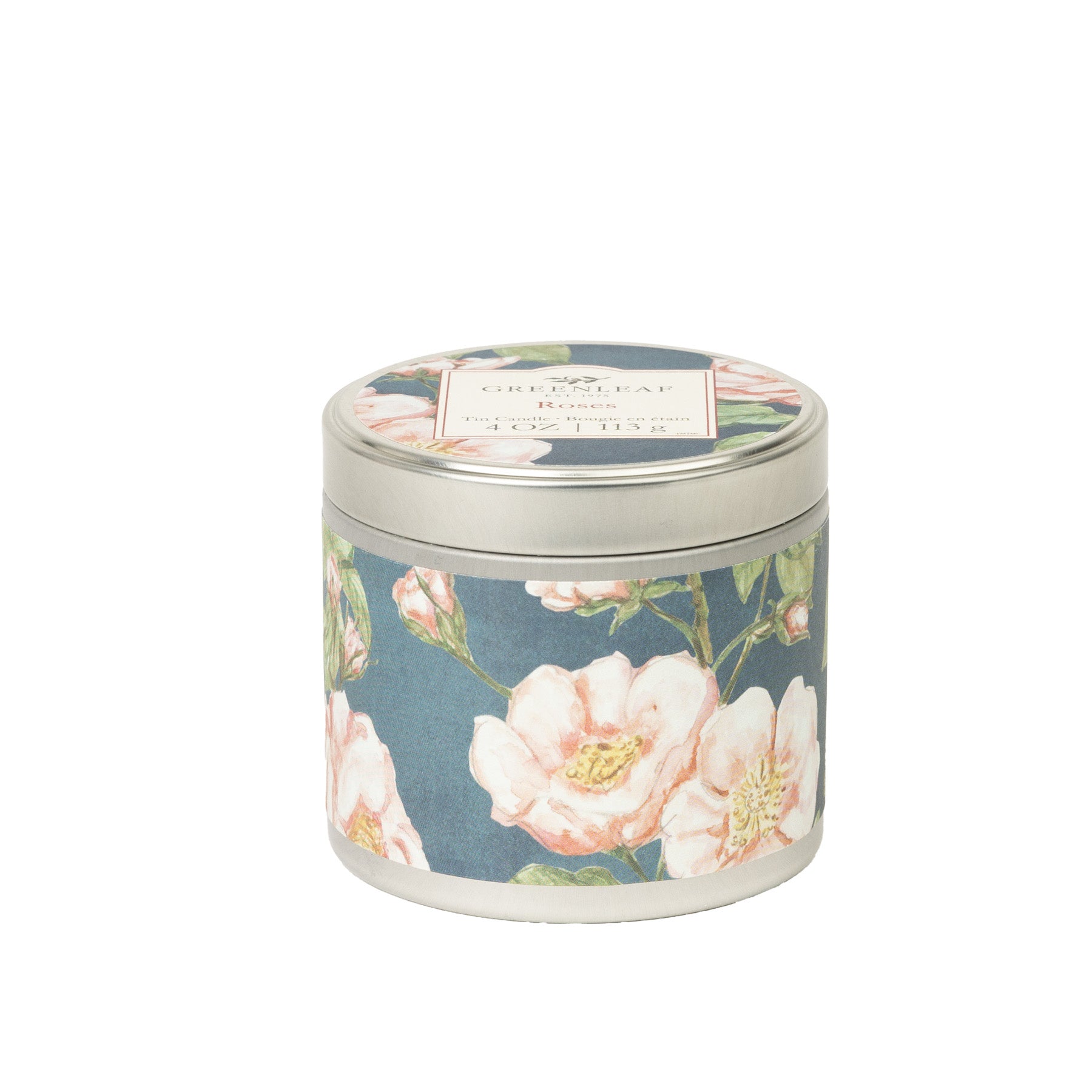 The Roses Tin Candle by Greenleaf Gifts is a round, portable tin candle with a lid, showcasing a blue background with white-pink floral designs. The top label highlights its soothing Roses fragrance.