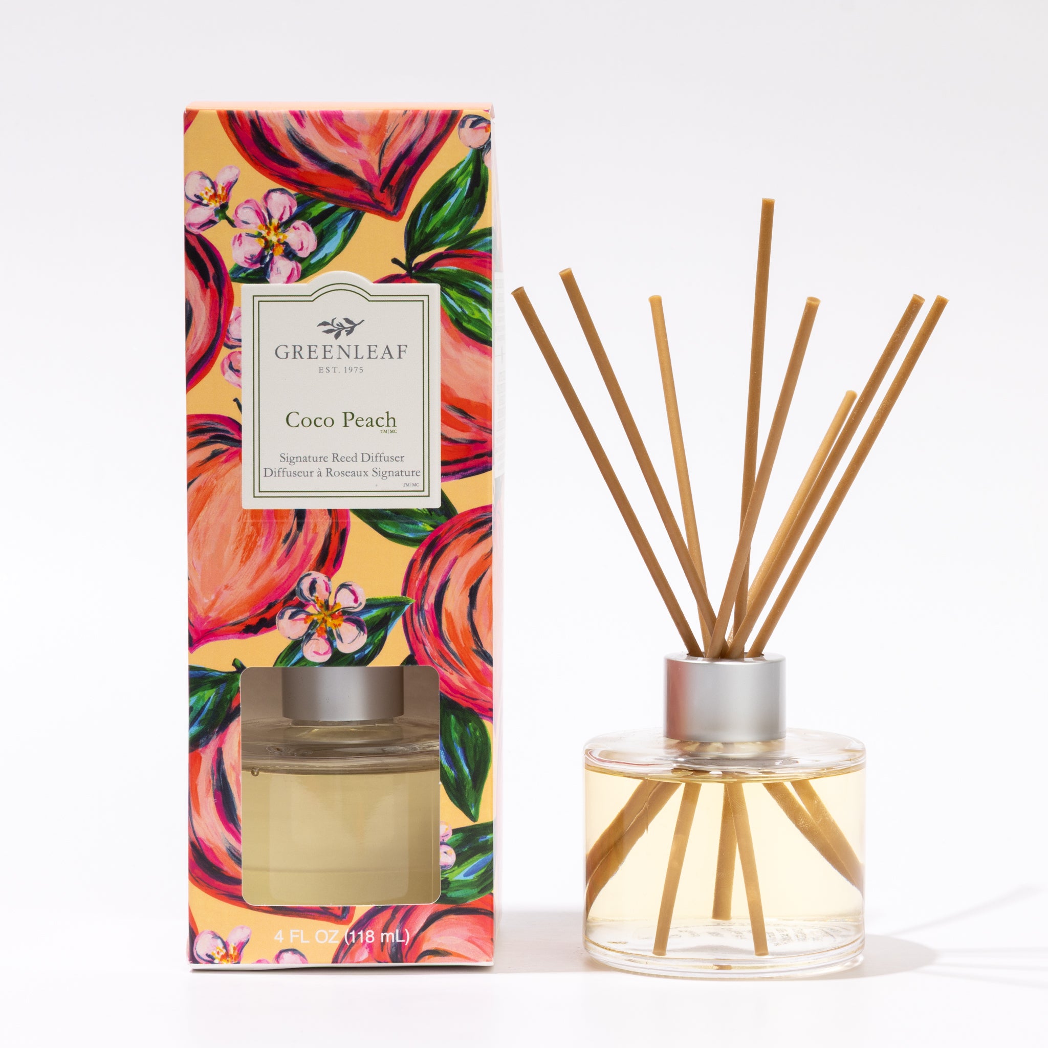 A Greenleaf Gifts Coco Peach Reed Diffuser with fiber reeds and a silver cap stands beside its decorative box adorned with peach and floral artwork, both set against a white background.