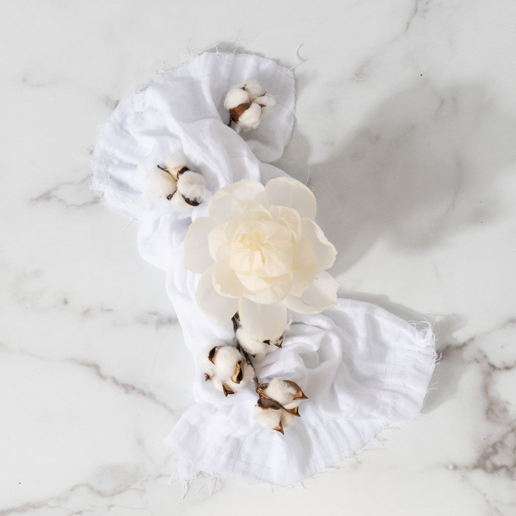 A white flower and cotton bolls are arranged on linen atop marble, evoking the elegant Classic Linen Flower Diffuser by Greenleaf Gifts, enhanced with a soothing fragrance oil.