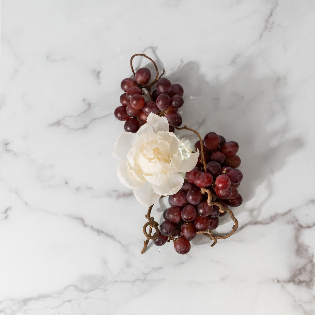 The Greenleaf Gifts Tuscan Vineyard Flower Diffuser features a sola paper flower resting atop a cluster of red grapes arranged on white marble.