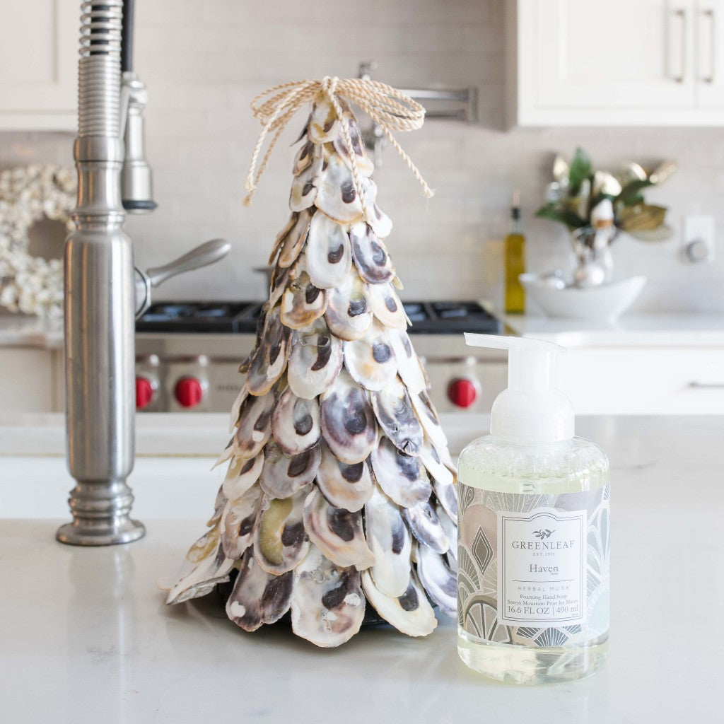 A decorative oyster shell tree sits on a kitchen counter next to a bottle of Haven Foaming Hand Soap by Greenleaf Gifts. Stainless steel appliances and light cabinets can be seen in the background.