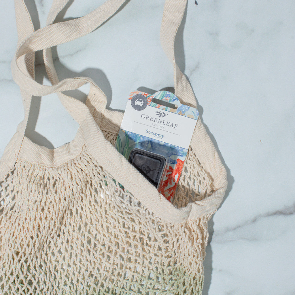 A cream mesh tote on a white surface holds a Greenleaf Gifts Seaspray fragrance sachet in the pocket—an ideal match for the Greenleaf Gifts Seaspray Auto Vent Clip, your next car air freshener.