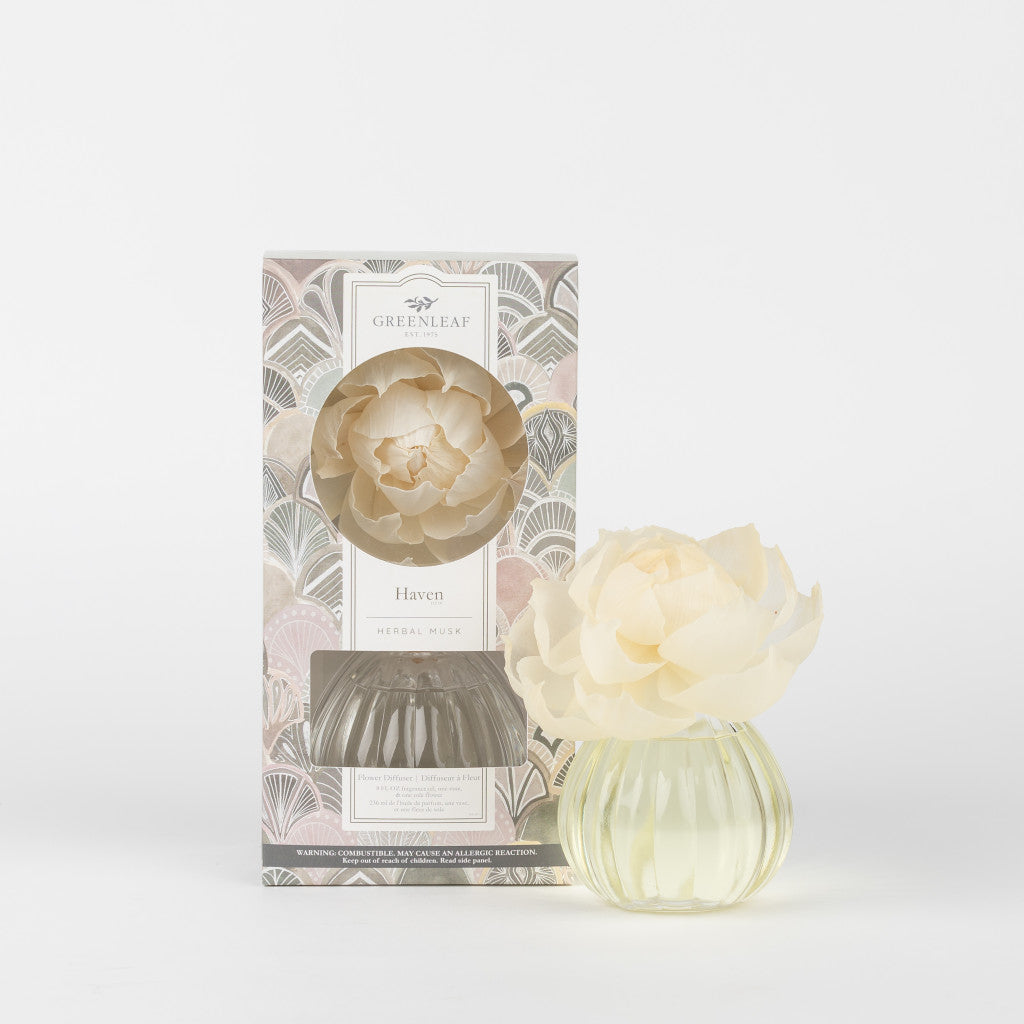 The Greenleaf Gifts Haven Flower Diffuser features a cream flower in a round glass vase and comes with a patterned box, bringing a soothing herbal musk scent to your space.