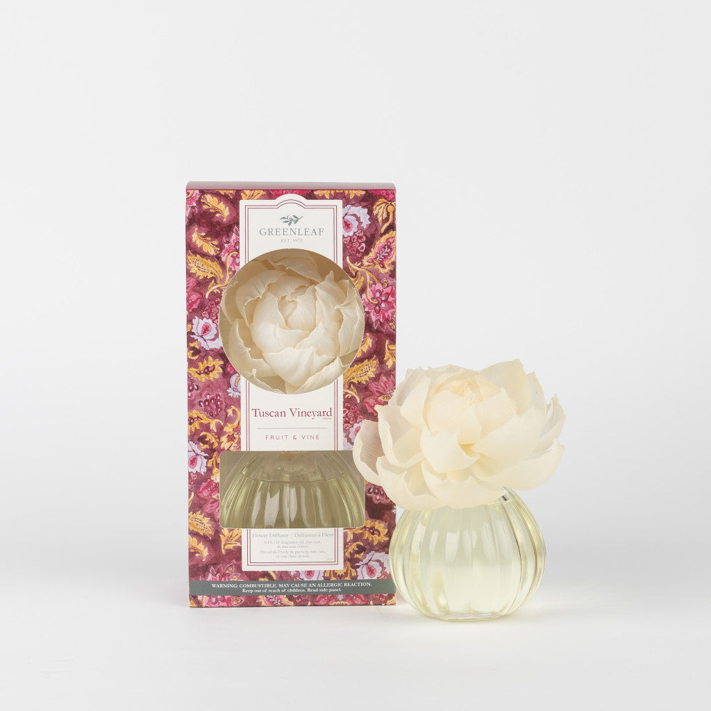The Greenleaf Gifts Tuscan Vineyard Flower Diffuser features a sola paper flower atop a clear glass vase, paired with its floral box. Fragrance oil fills the air, all displayed on a simple white background.
