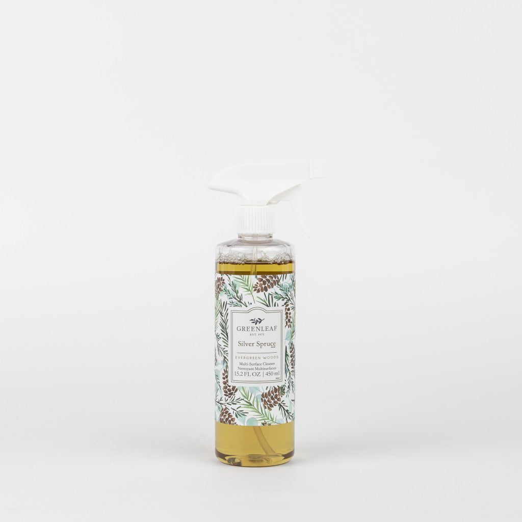 A clear spray bottle filled with yellow liquid, labeled Greenleaf Gifts Silver Spruce Multi-Surface Cleaner, features a decorative label with pinecones and green leaves—ideal for freshening non-porous surfaces.