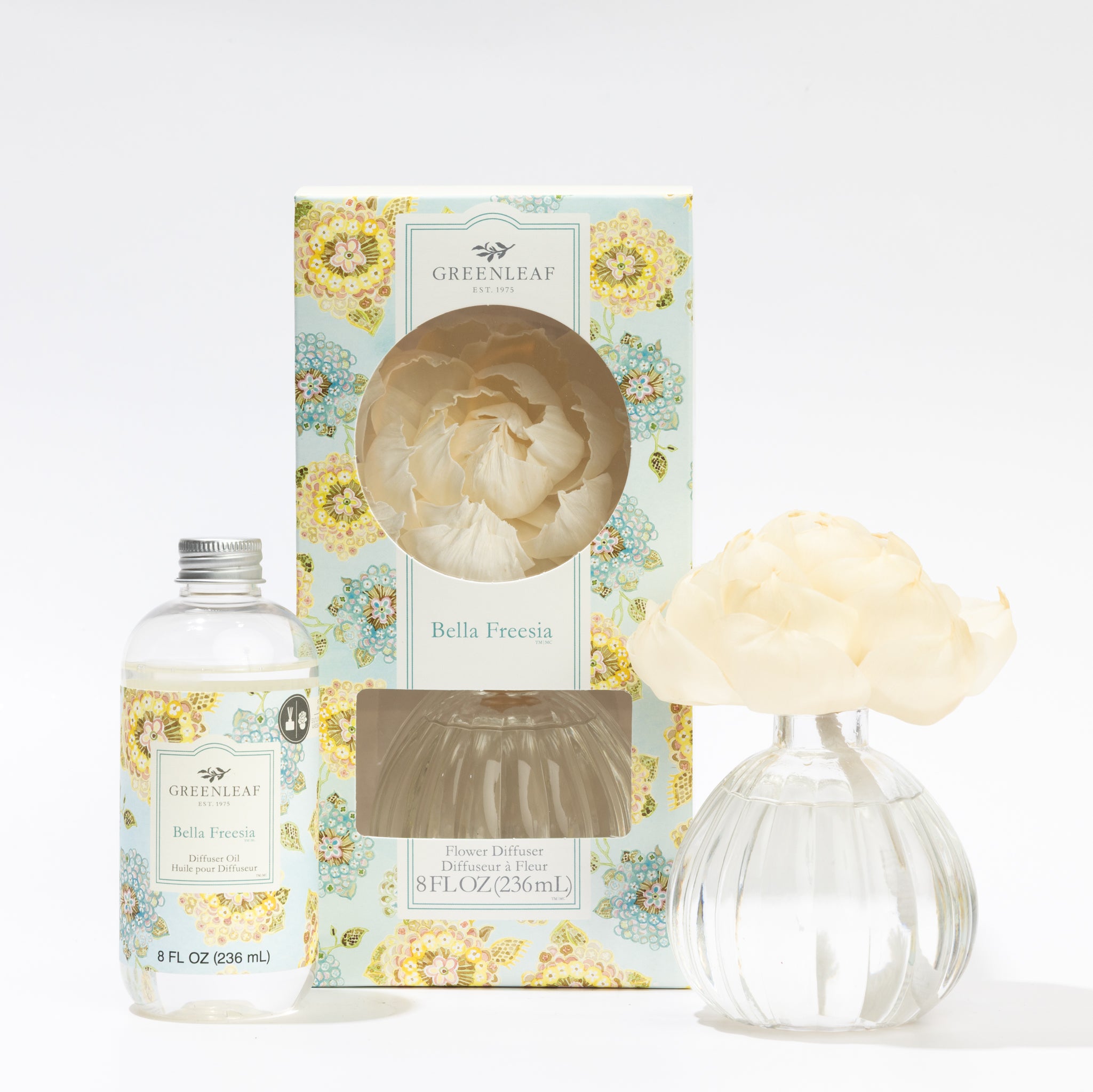 The Fast Bundle Bella Freesia Flower Diffuser & Fragrance Oil Refill includes a floral box, clear oil bottle, and round glass vase with white flower—ideal for adding long-lasting fragrance to any space.