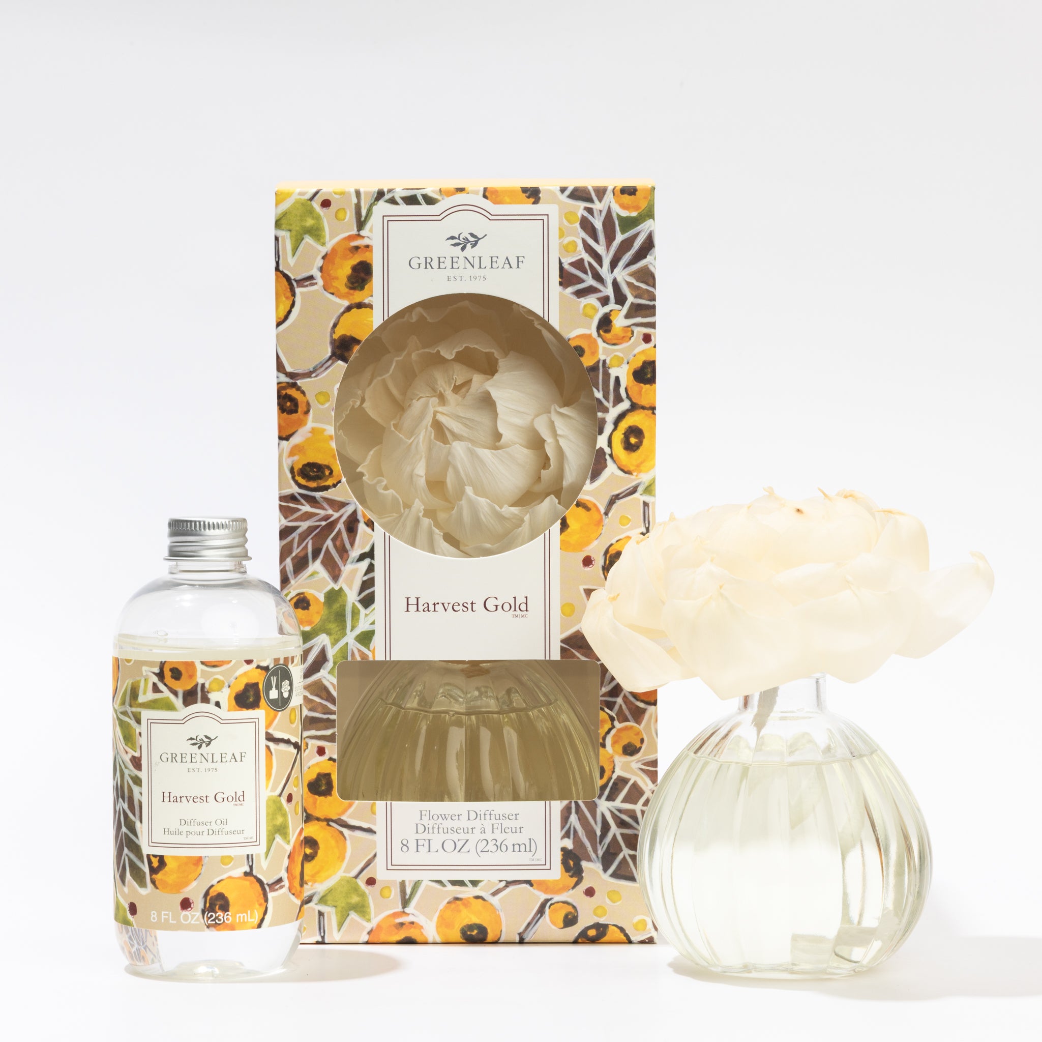 The Fast Bundle Harvest Gold Flower Diffuser & Fragrance Refill Oil includes Greenleaf fragrance oil, a floral box, a clear glass bottle with liquid, and a white flower-shaped diffuser in a round vase, shown on a white background.