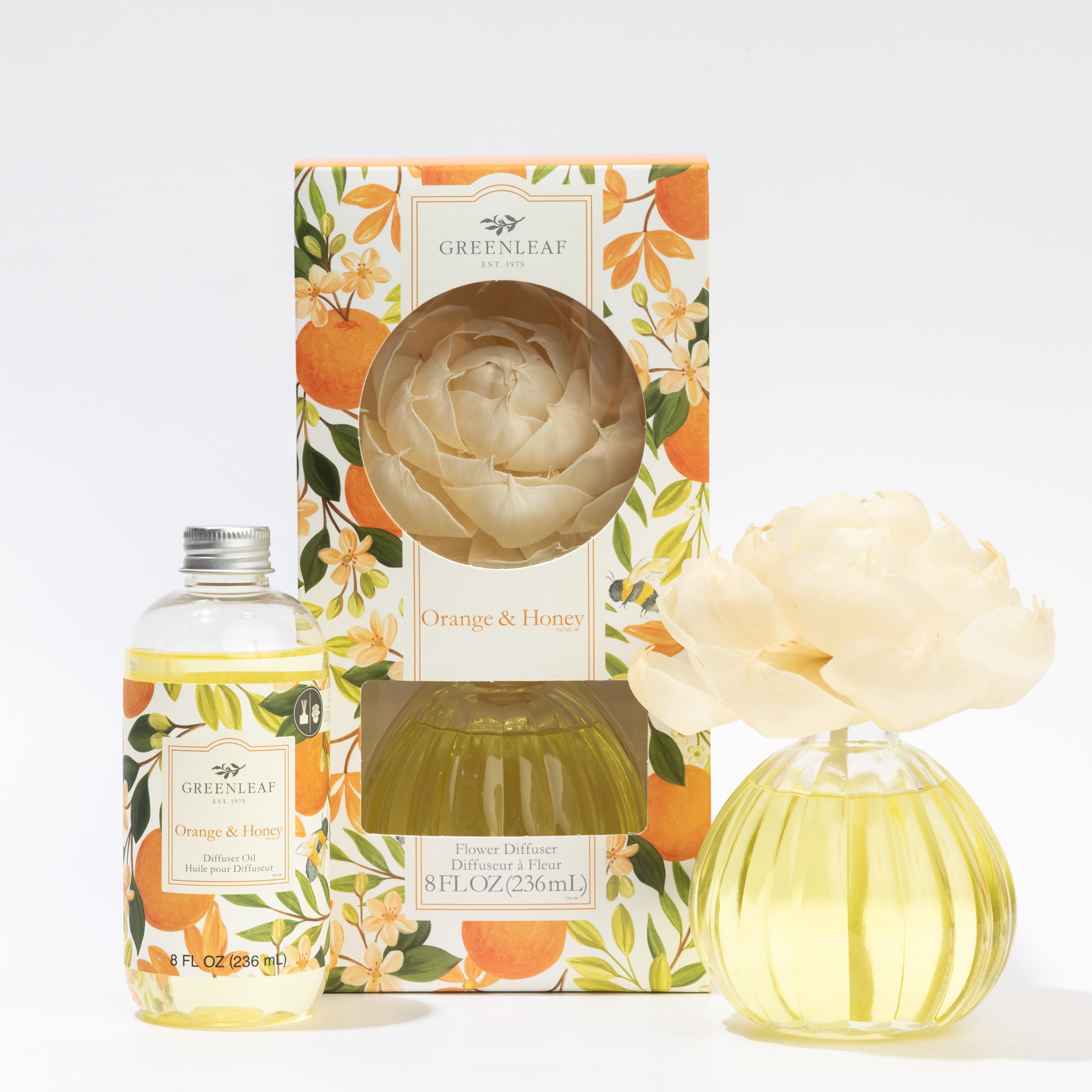The Fast Bundle Orange & Honey Flower Diffuser & Fragrance Refill Oil set features a round glass vase with a light flower, floral-patterned box, and light yellow oil. Perfect as a gift or for use as a diffuser refill.