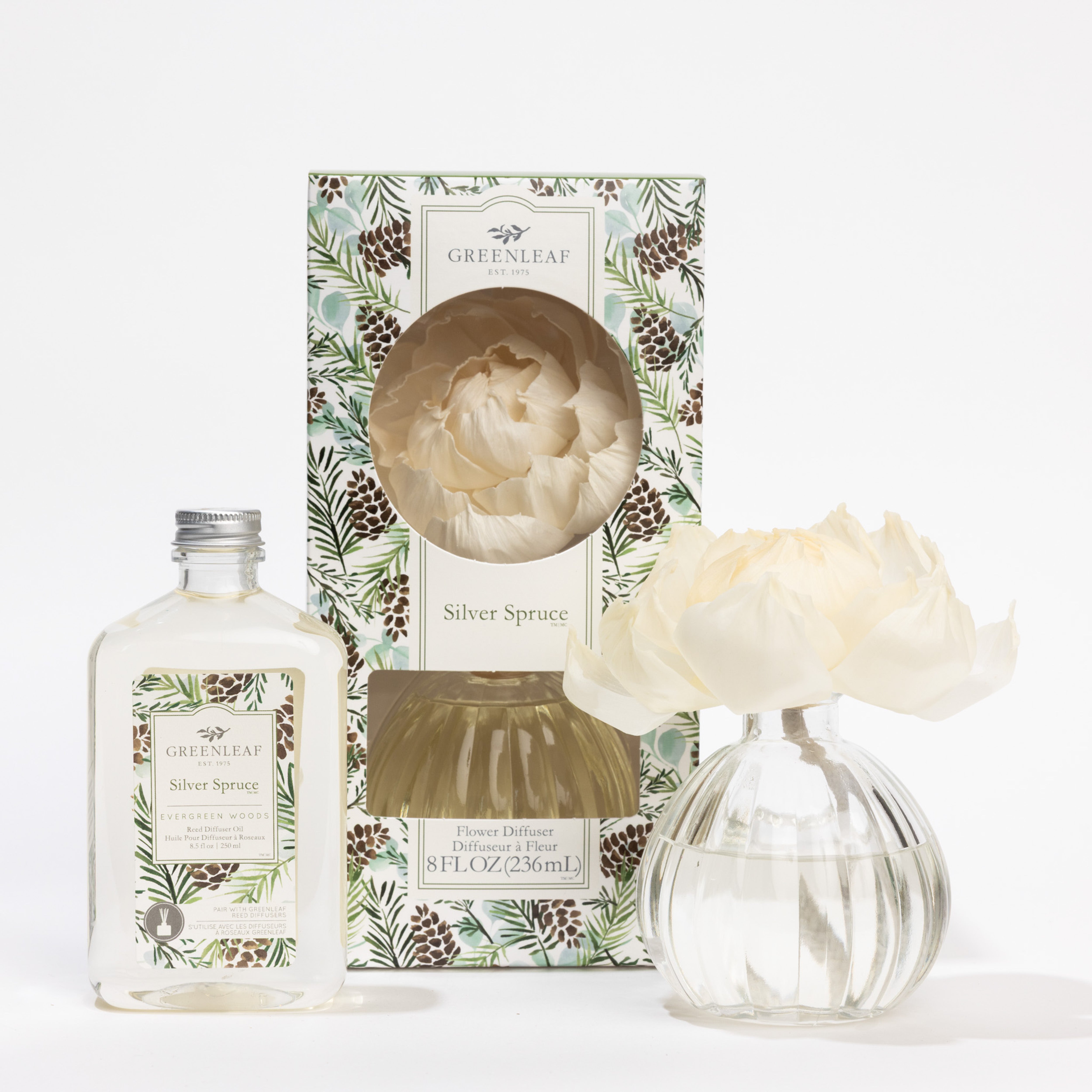 The Fast Bundle Silver Spruce Flower Diffuser & Fragrance Refill Oil set includes a decorative box with pinecone and leaf accents, a glass vase with a cream artificial flower, and clear Greenleaf fragrance oil.