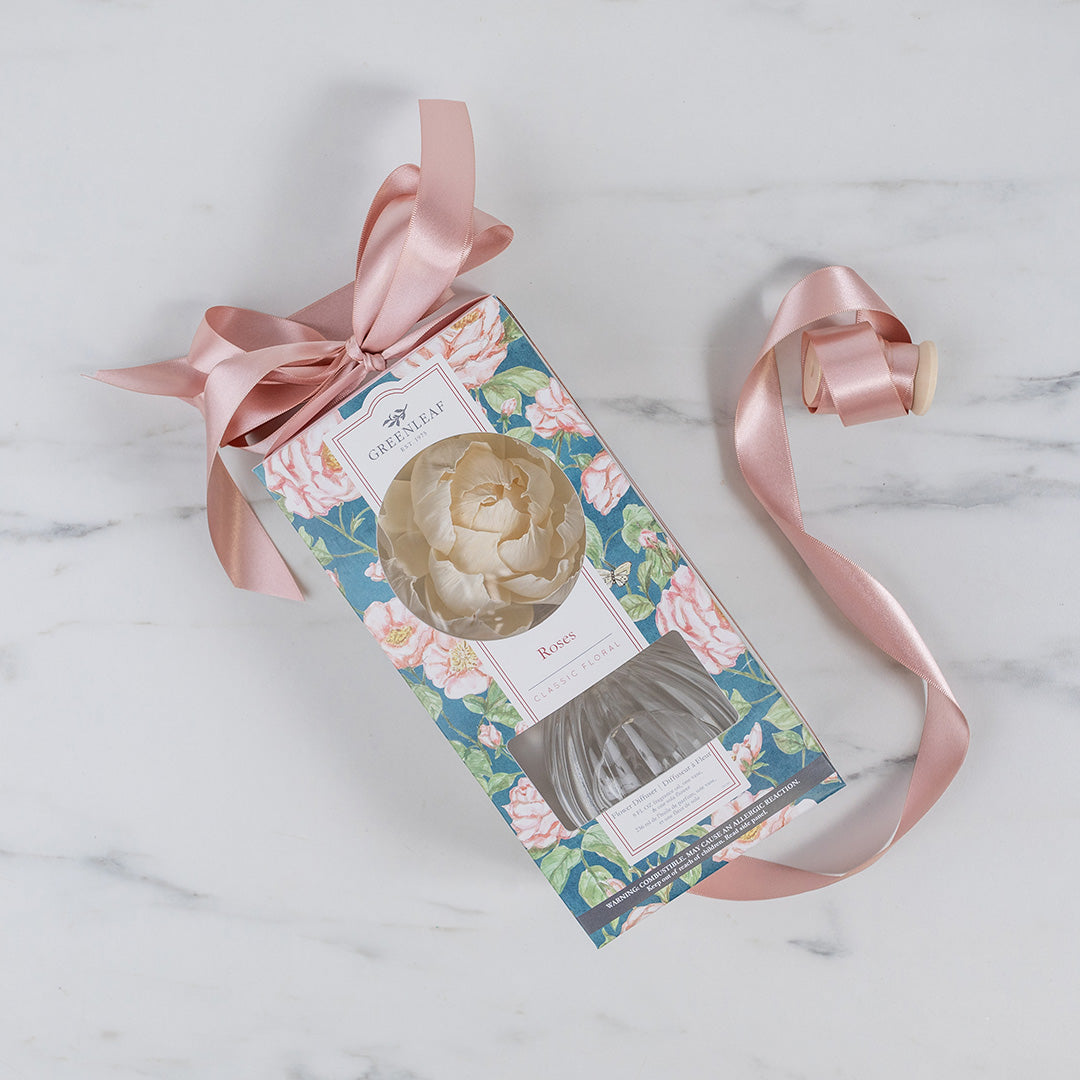 The Roses Flower Diffuser by Greenleaf Gifts features a floral-patterned bag with a pink ribbon, sola paper flower, and “Rosé” label. Perfect for pairing with fragrance oil and gifting someone special. Displayed on white marble.