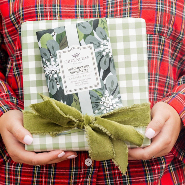 Person wearing a red plaid shirt holding a gift wrapped in green paper with a bow.