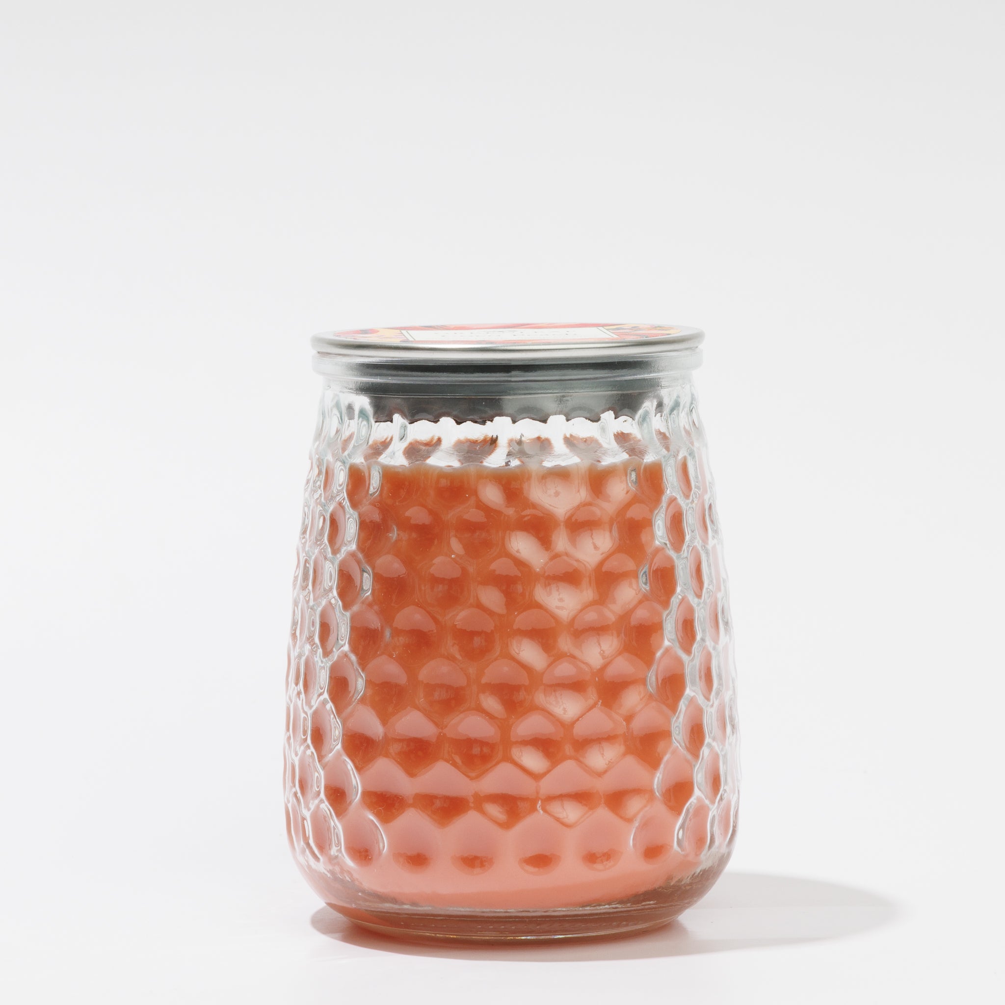 A clear glass jar with a honeycomb pattern, filled with pinkish-orange Coco Peach Signature Candle by Greenleaf Gifts, and sealed with a metal lid, set against a plain white background.