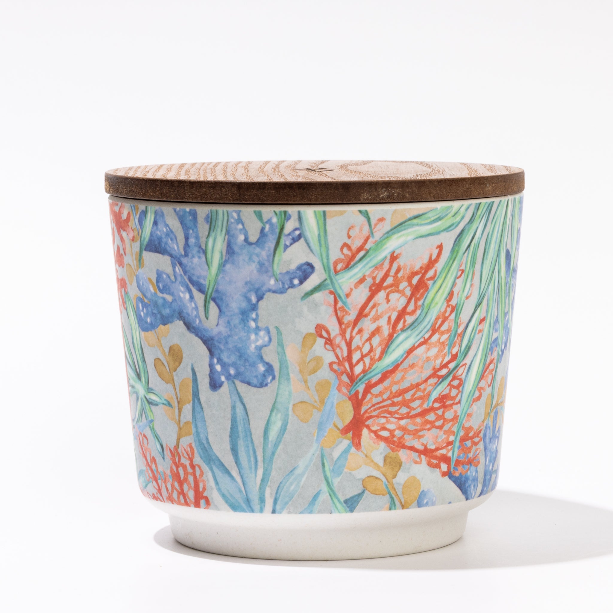 The Greenleaf Gifts Seaspray Patterned 3 Wick Candle comes in a colorful ceramic container with a wooden lid, featuring a vibrant hand-painted floral and leafy design—ideal for storing small treasures after the candle is used.