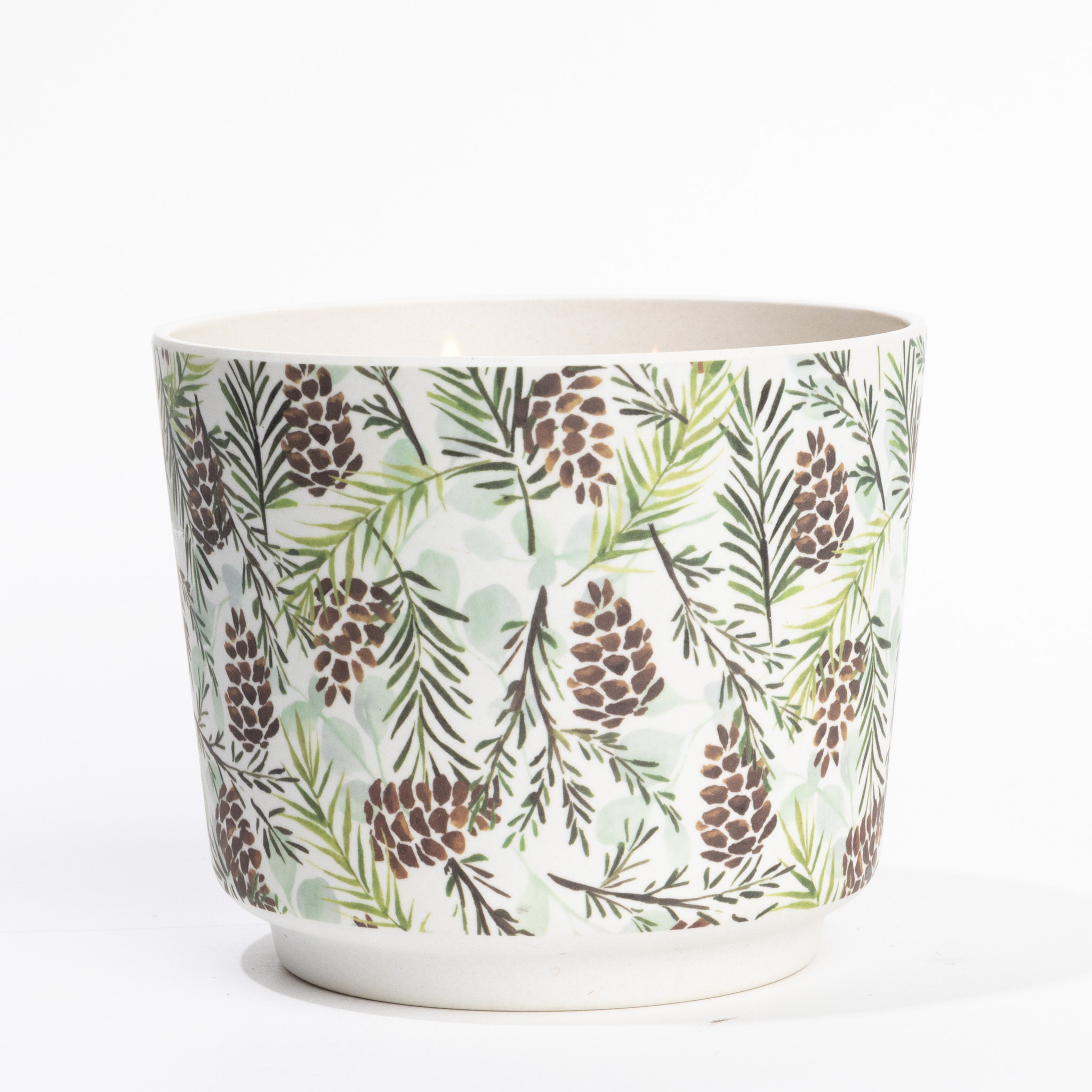 The Silver Spruce Patterned 3 Wick Candle by Greenleaf Gifts features pinecones and green pine needles on a white background, evoking the fragrance of silver spruce, and is shown against a plain white surface.