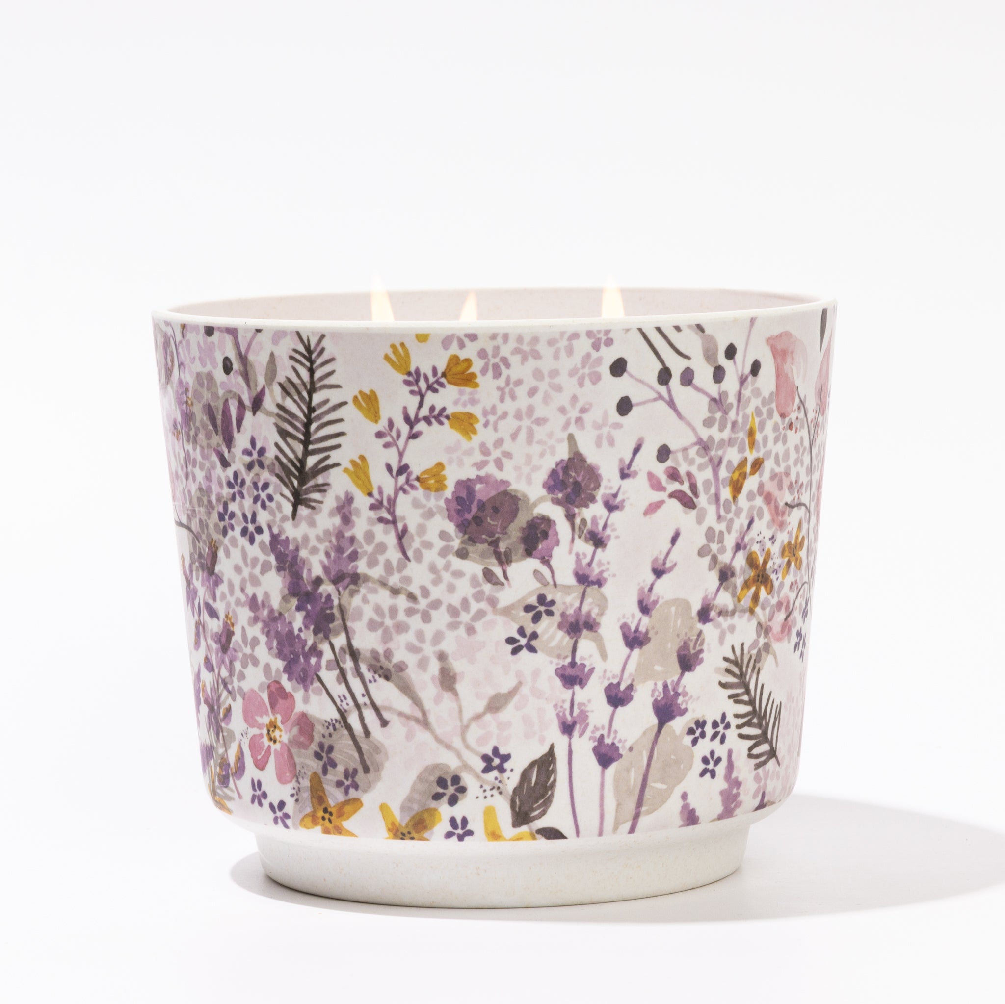 The Lavender Patterned 3 Wick Candle by Greenleaf Gifts glows in a round container with a purple, yellow, and green floral pattern on white—perfect for patterned candle fans.