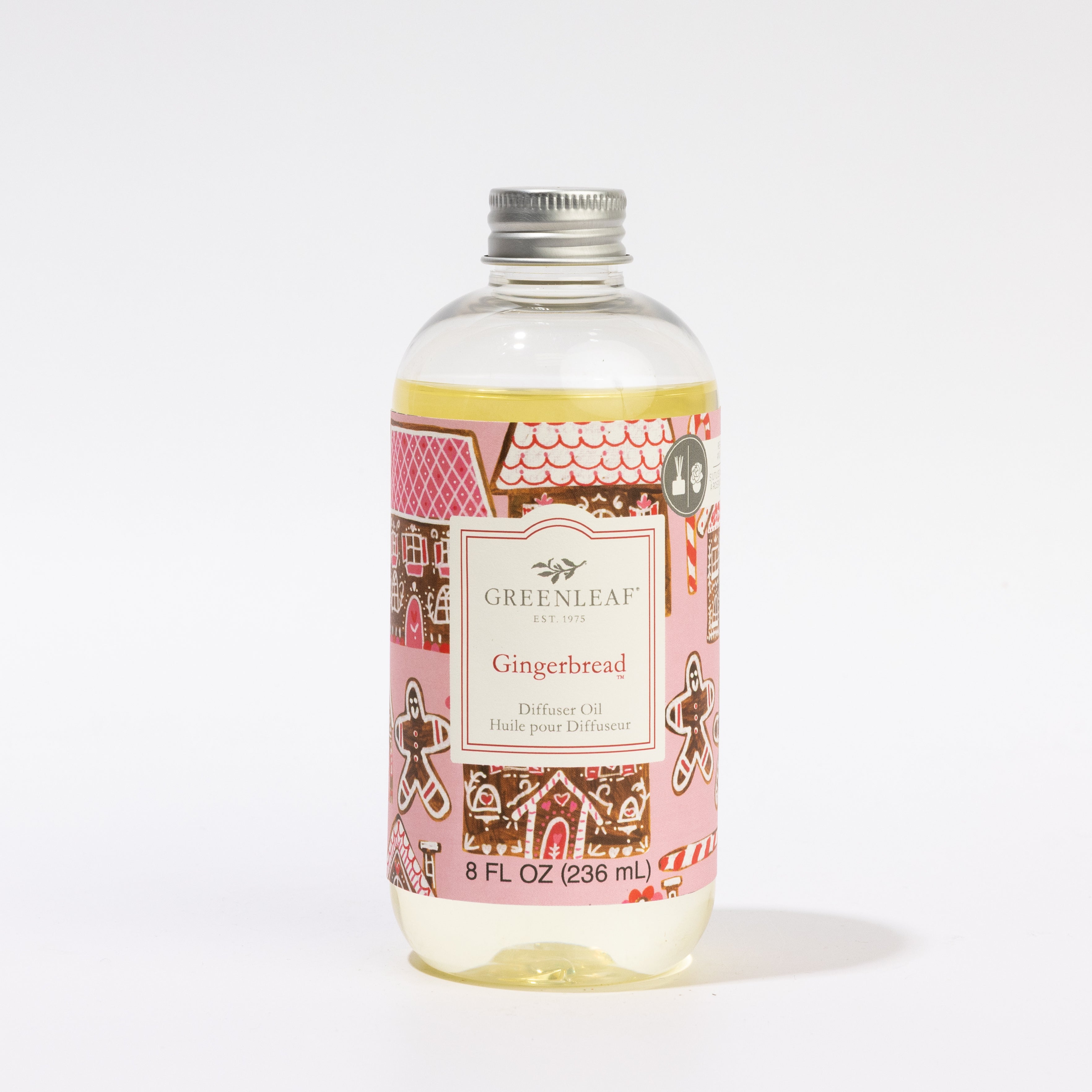 A clear 8 oz bottle of Greenleaf Gifts Gingerbread Diffuser Refill Oil features a silver cap and label with gingerbread house and cookie designs, providing a festive scent that lasts up to 30 days.