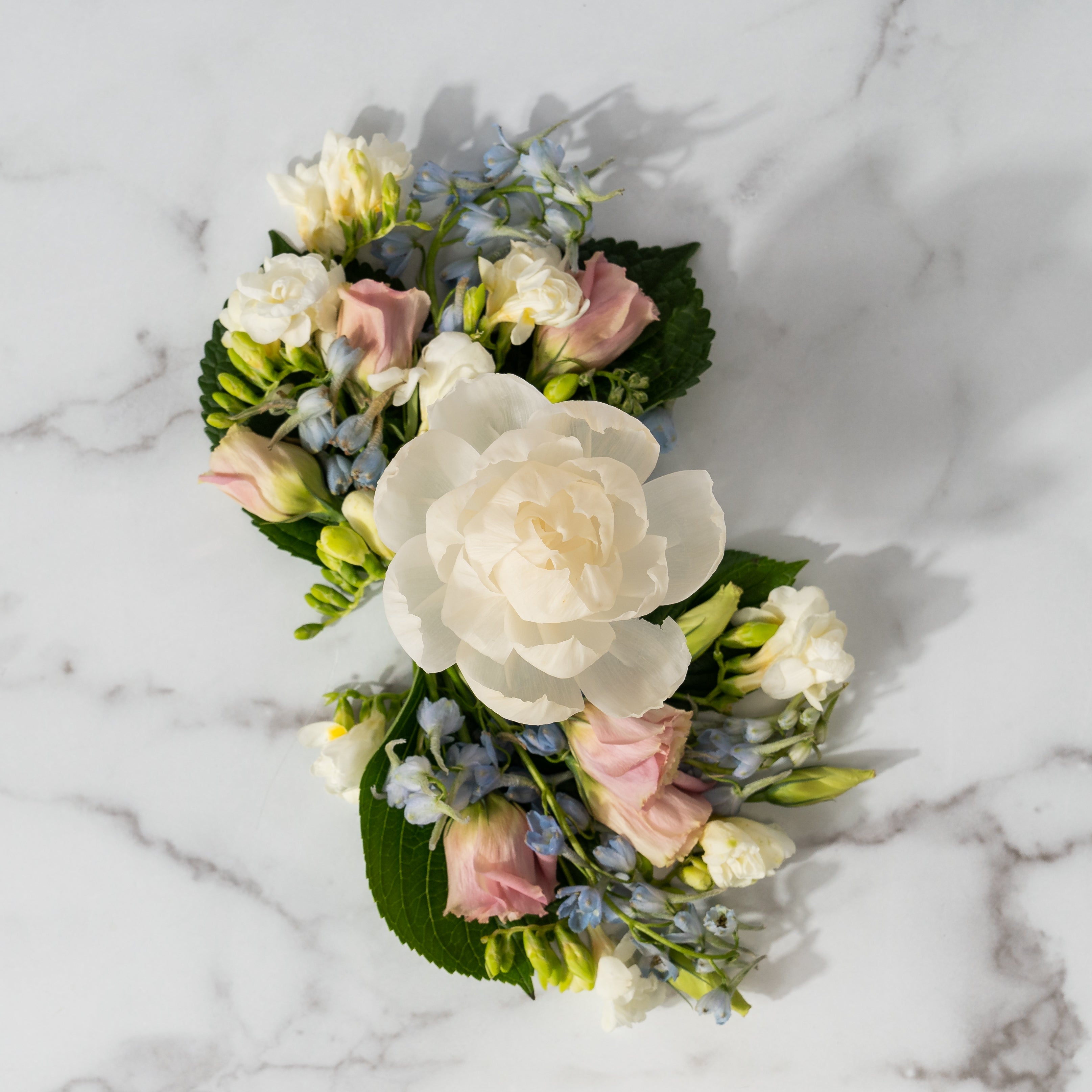 The Bella Freesia Flower Diffuser by Greenleaf Gifts features a large white rose surrounded by pale pink, white, and light blue blooms with green leaves on marble. Enjoy its 8 oz size for up to 60 days of lasting beauty.