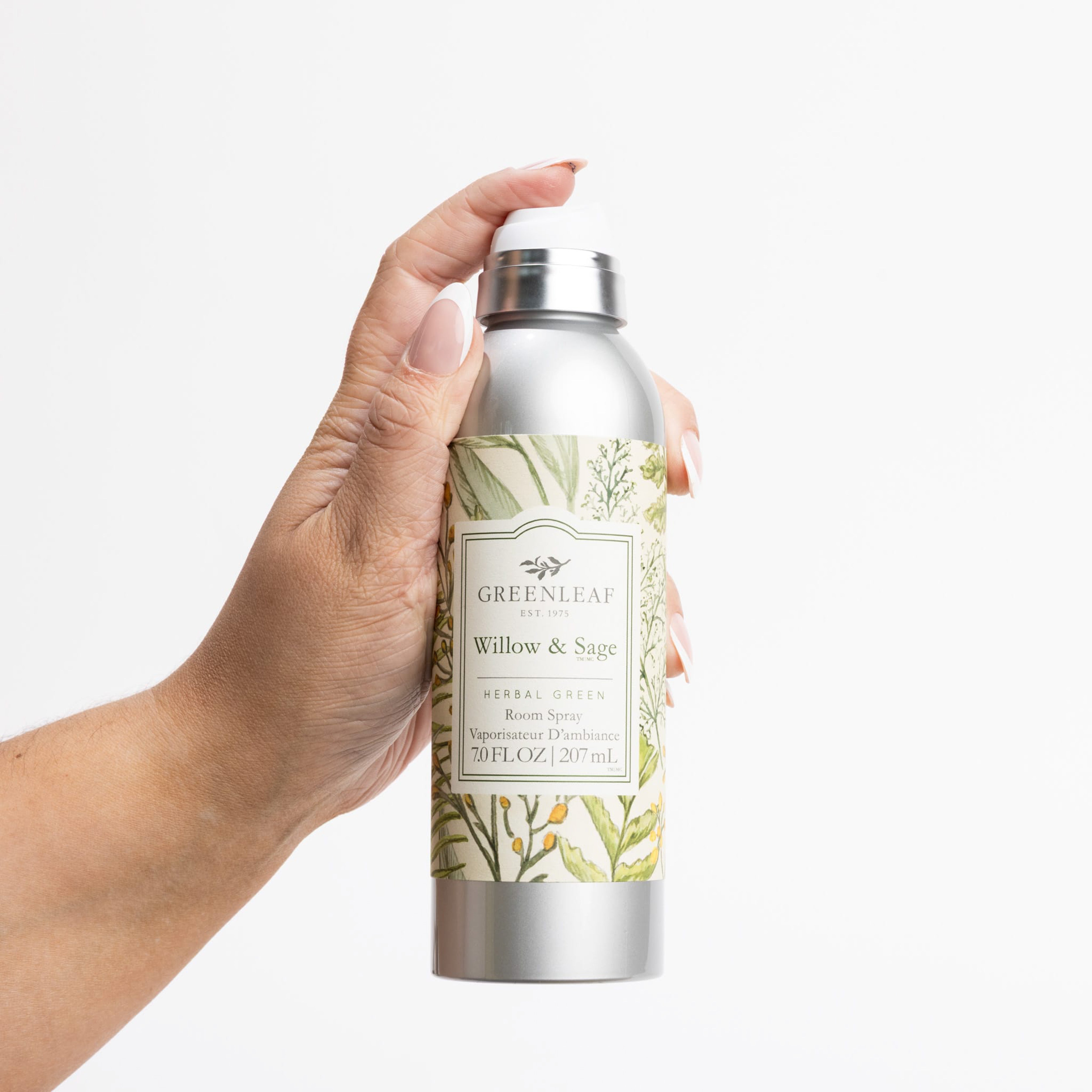 A hand holds a silver spray bottle labeled “Willow & Sage Room Spray” from Greenleaf Gifts, featuring a green botanical design on white and highlighting the signature Willow & Sage fragrance.