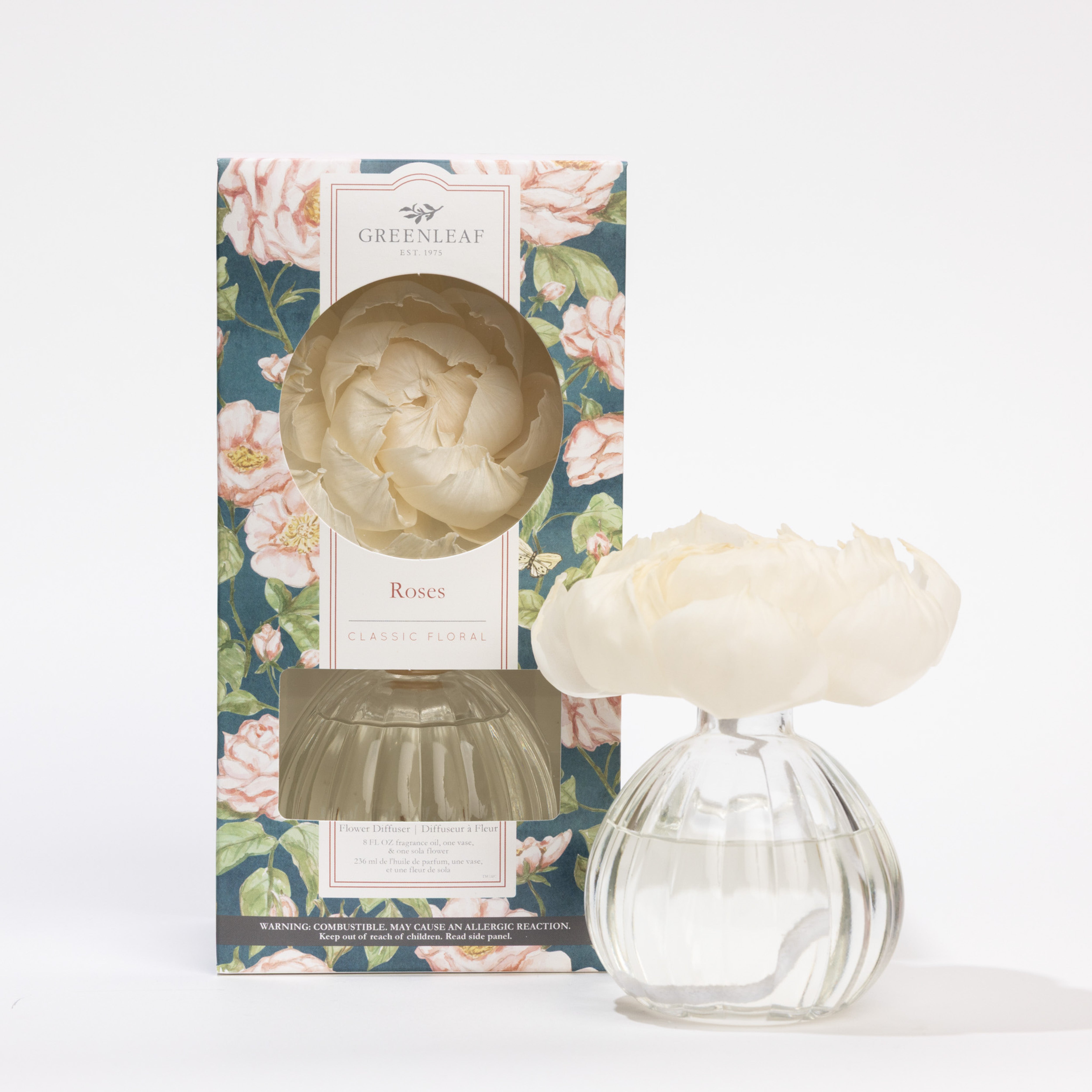 A Greenleaf Gifts Flower Diffuser-Roses (8 oz) with a white flower on top is displayed in front of its floral box. The label reads “Roses, Classic Floral,” and the scent lasts up to 60 days.